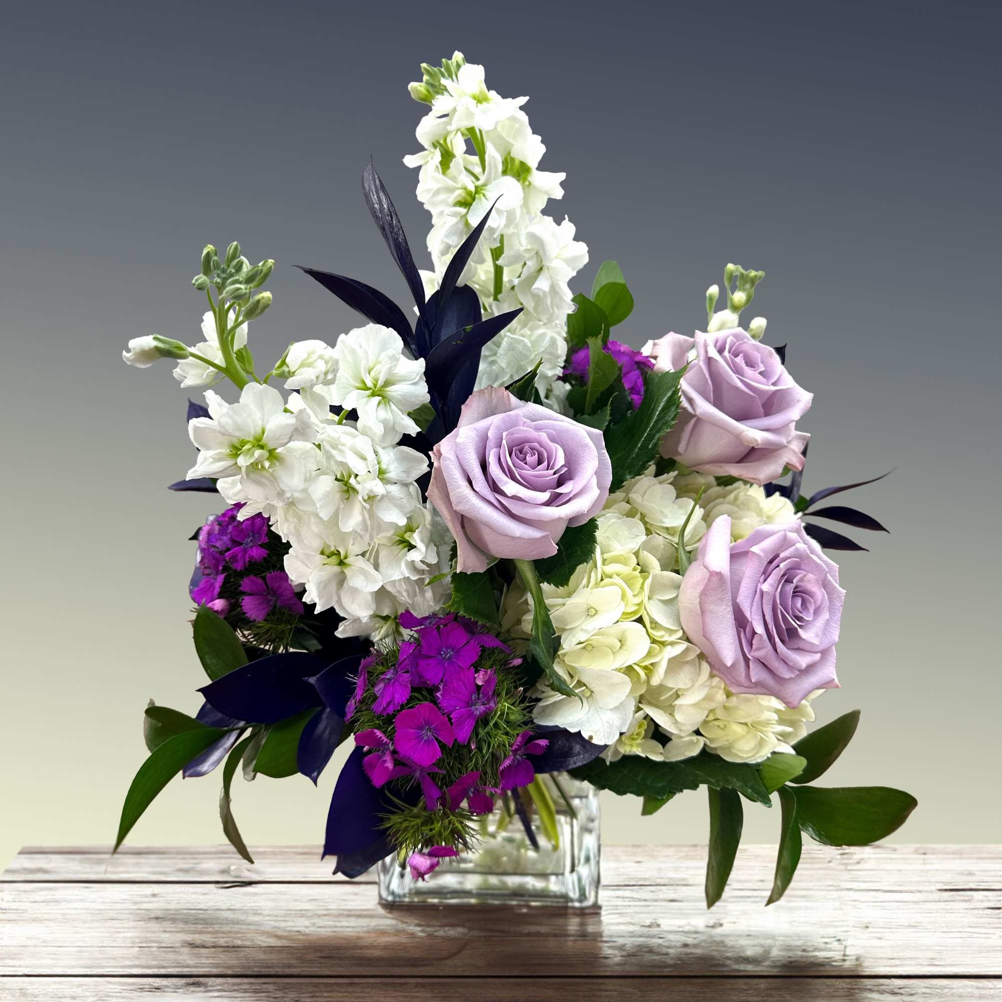 Lavender roses and white flowers in a clear glass vase