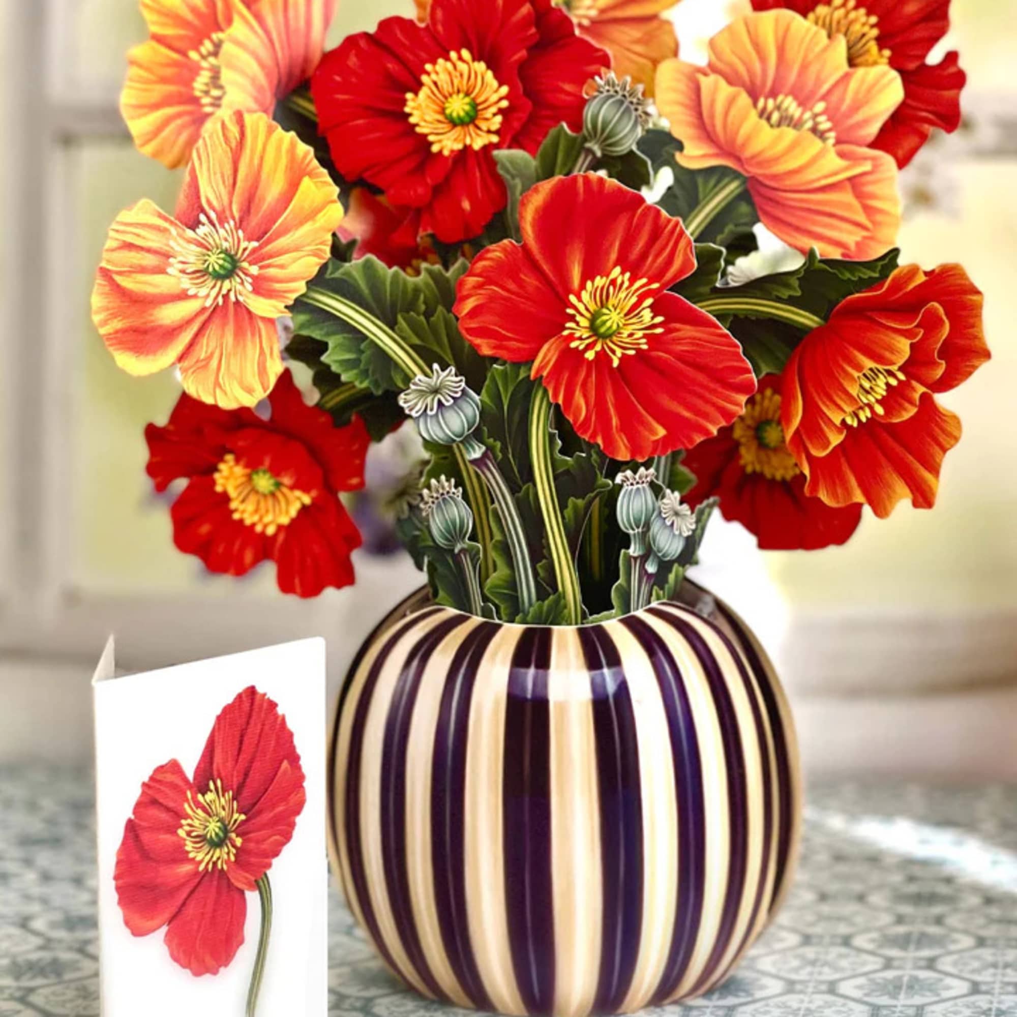 Bouquet of red and orange poppy-like flowers in a striped vase with a card