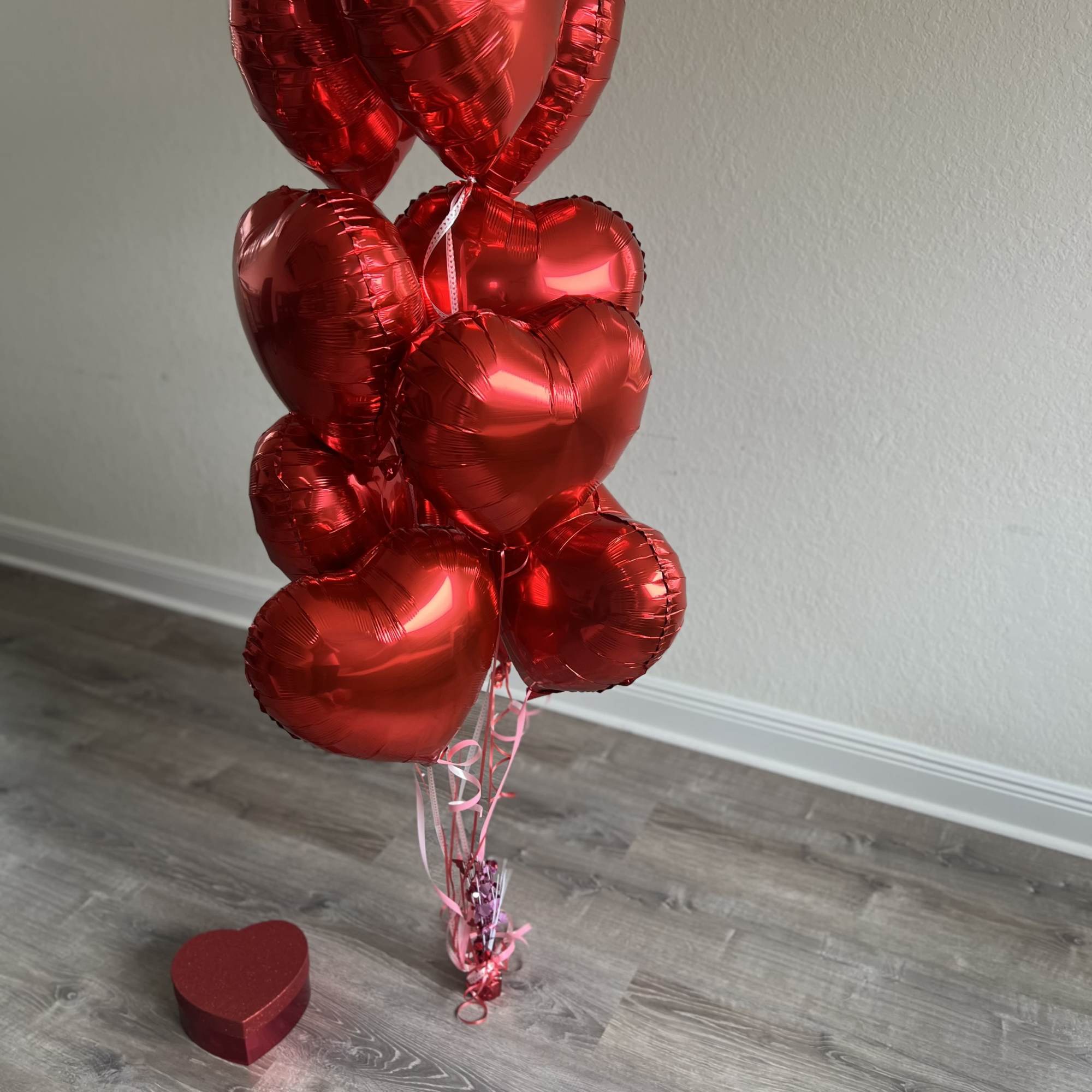 Cluster of red heart-shaped balloons with a small heart gift box on the floor