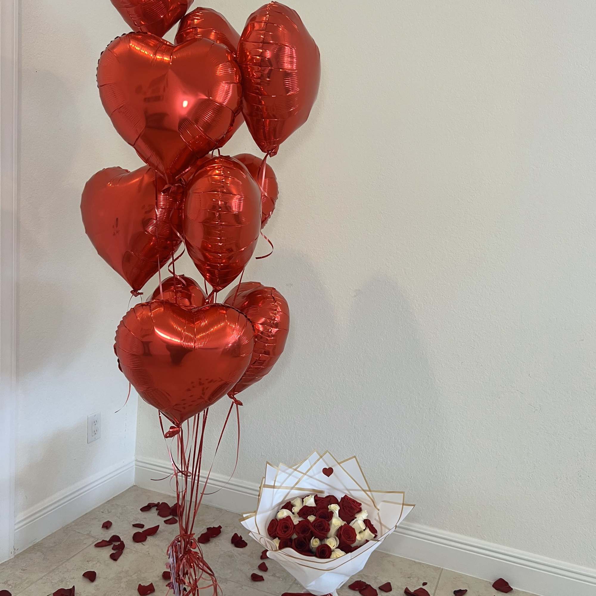 Red heart balloons beside a bouquet of red and white roses