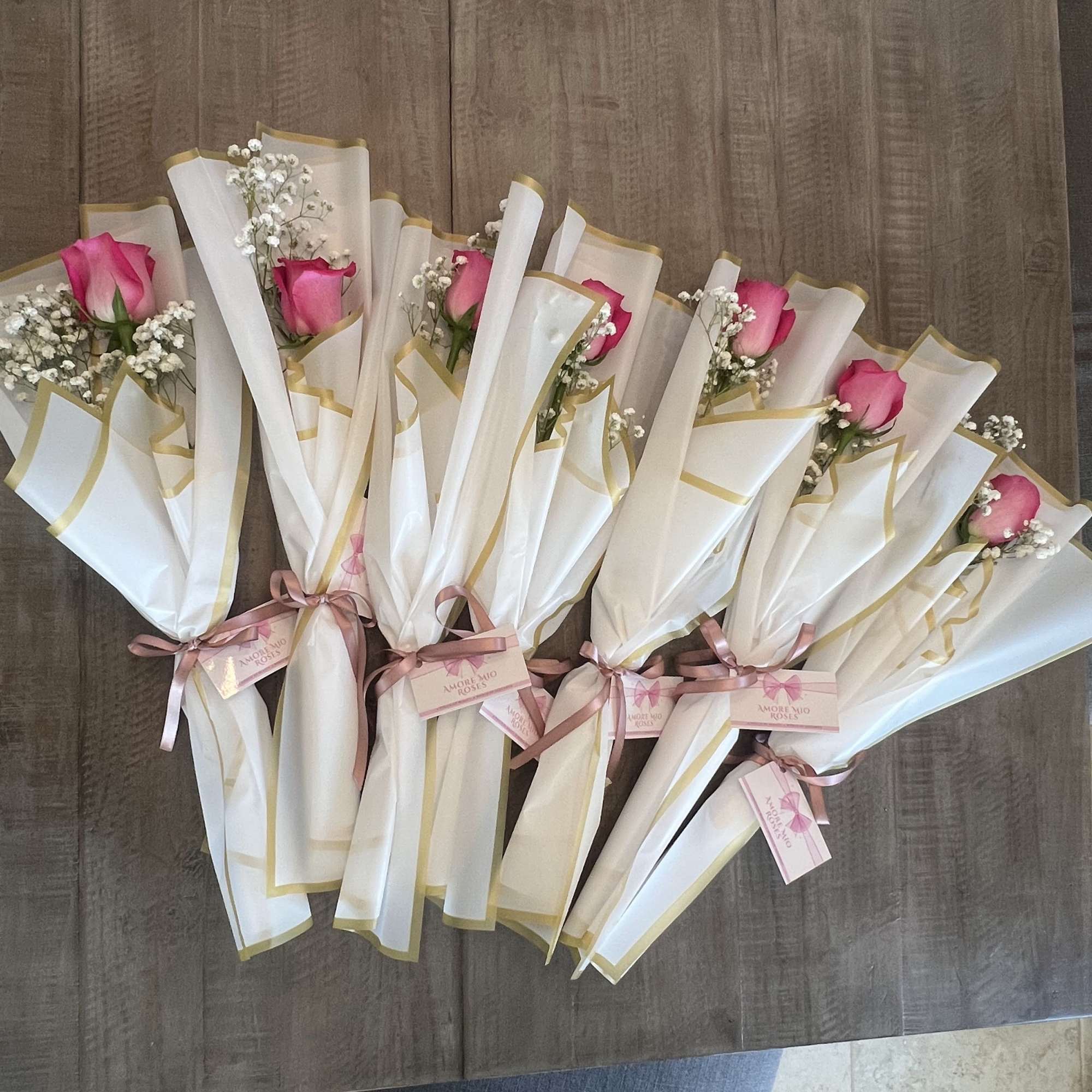Pink roses wrapped in white paper with gold trim and ribbon