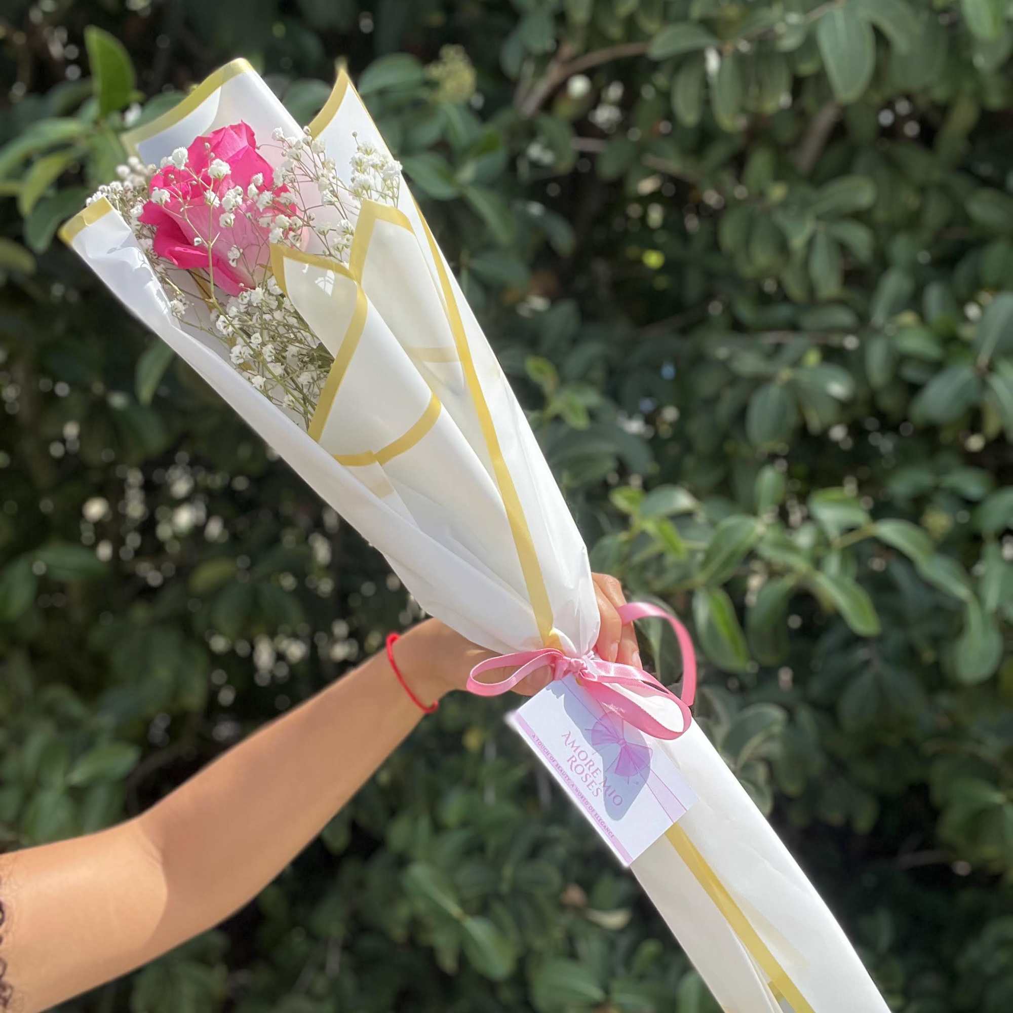 Handheld bouquet of pink roses wrapped in white paper with a pink ribbon