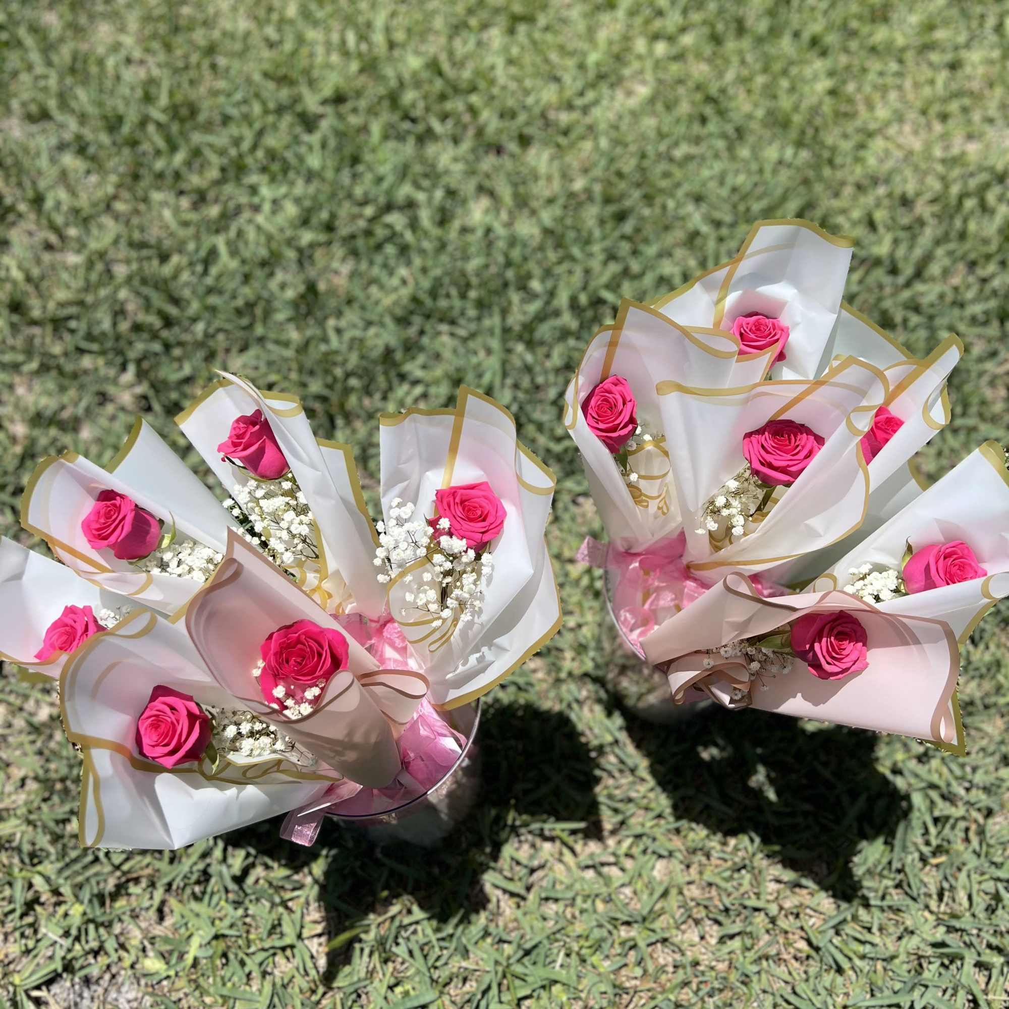 Several small bouquets of pink roses wrapped in white paper on grass.