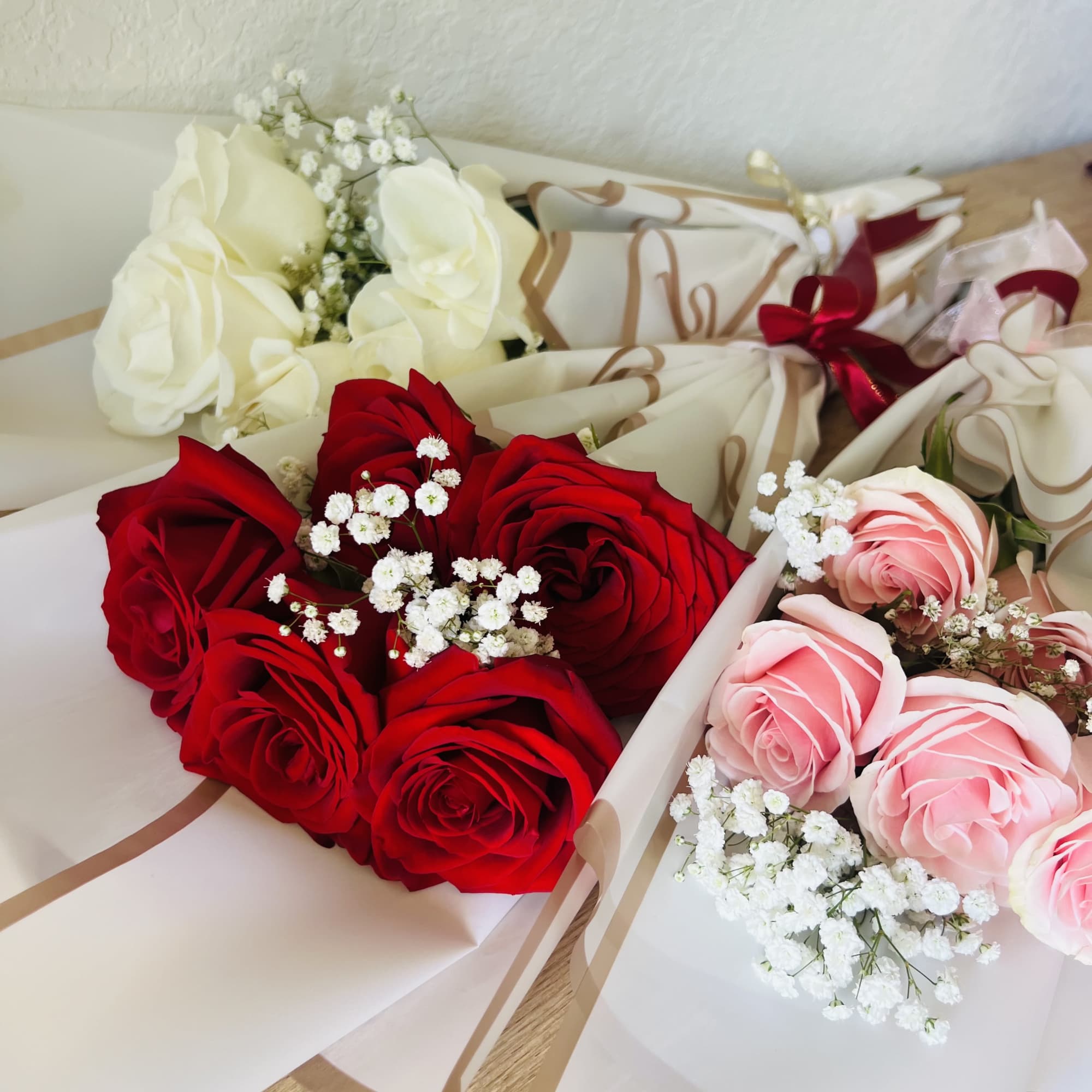 Three wrapped rose bouquets in red, pink, and white