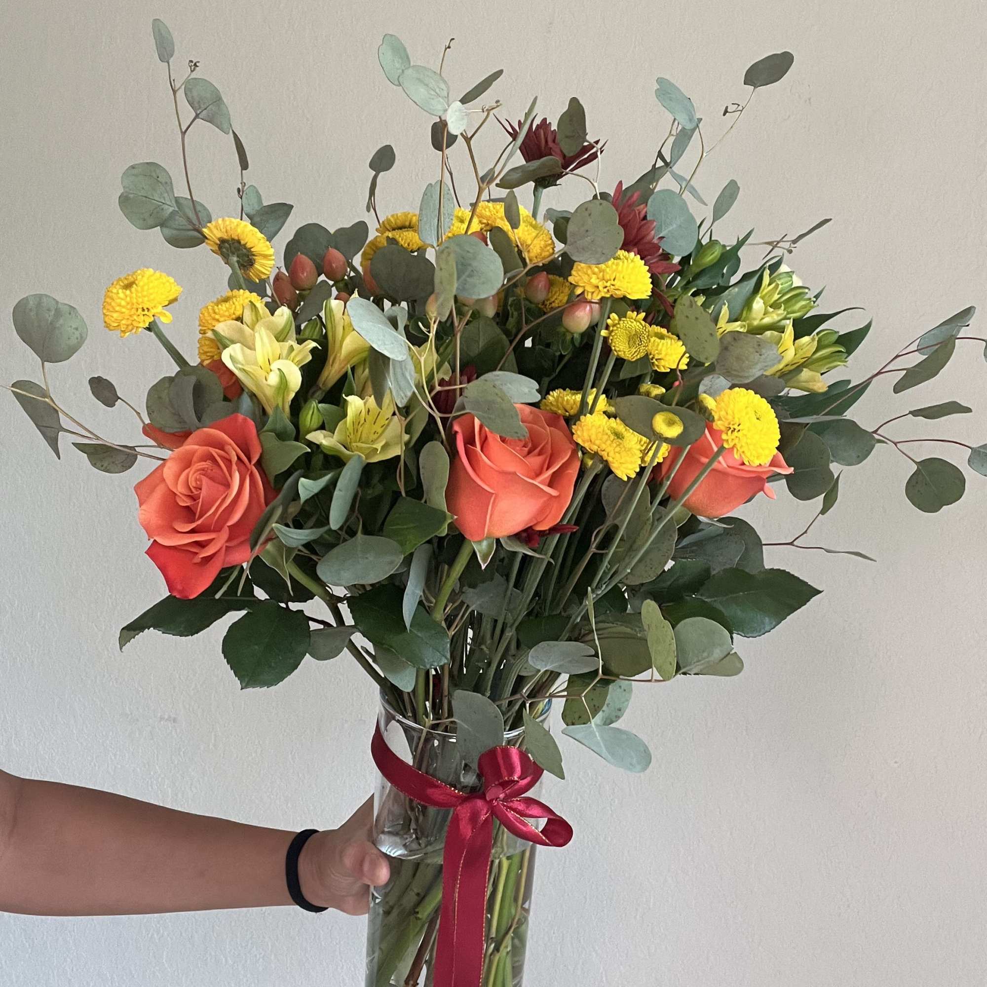 Bouquet of coral roses and yellow flowers in a glass vase with a ribbon