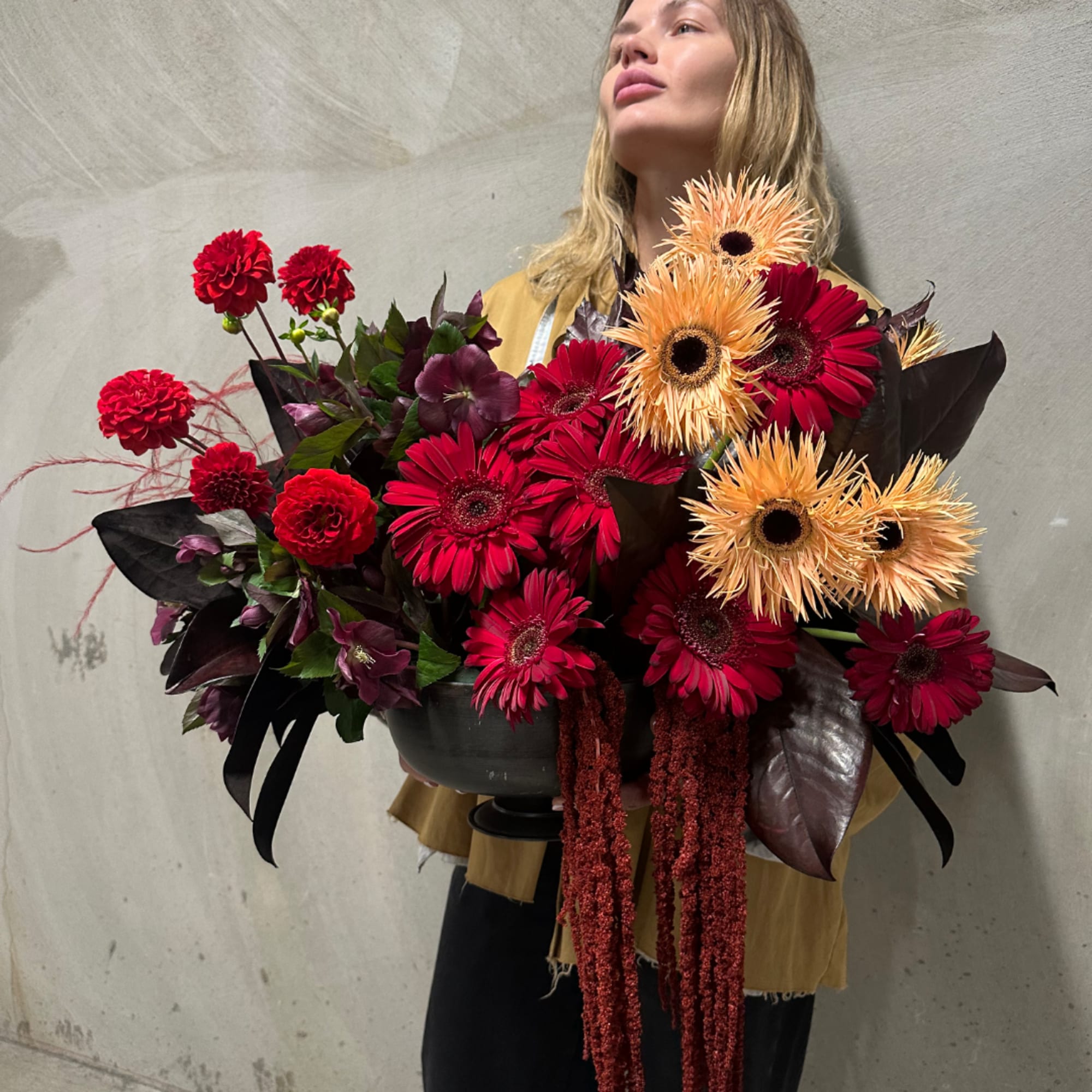 Woman holding a large bouquet of red and peach flowers in a dark container