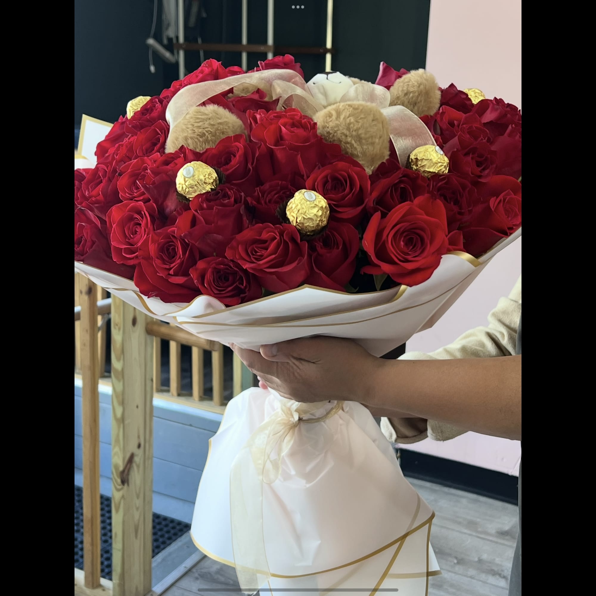 Large bouquet of red roses with gold-wrapped chocolates and beige pom-pom accents