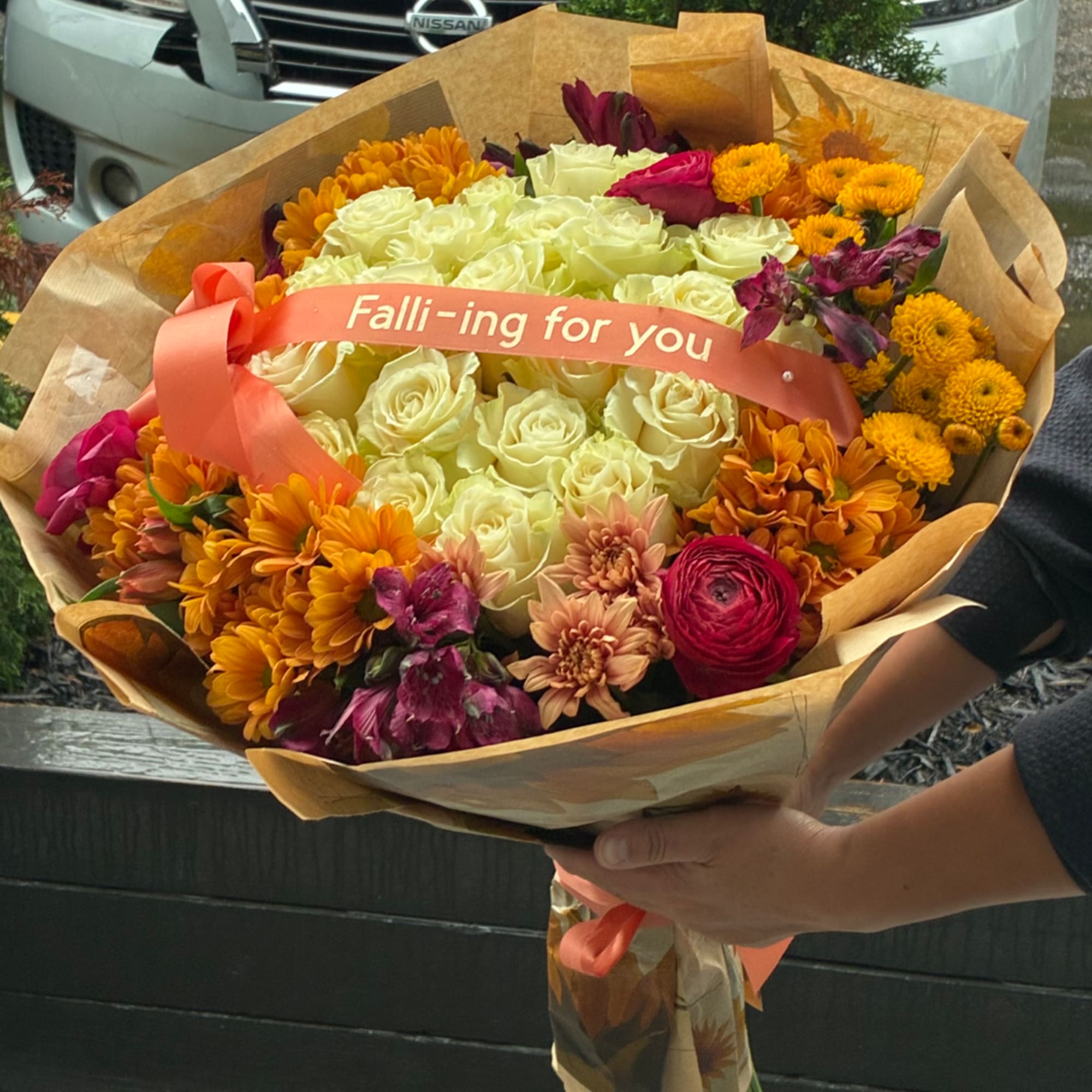 Handheld bouquet of cream roses, orange mums, and pink flowers with a ribbon