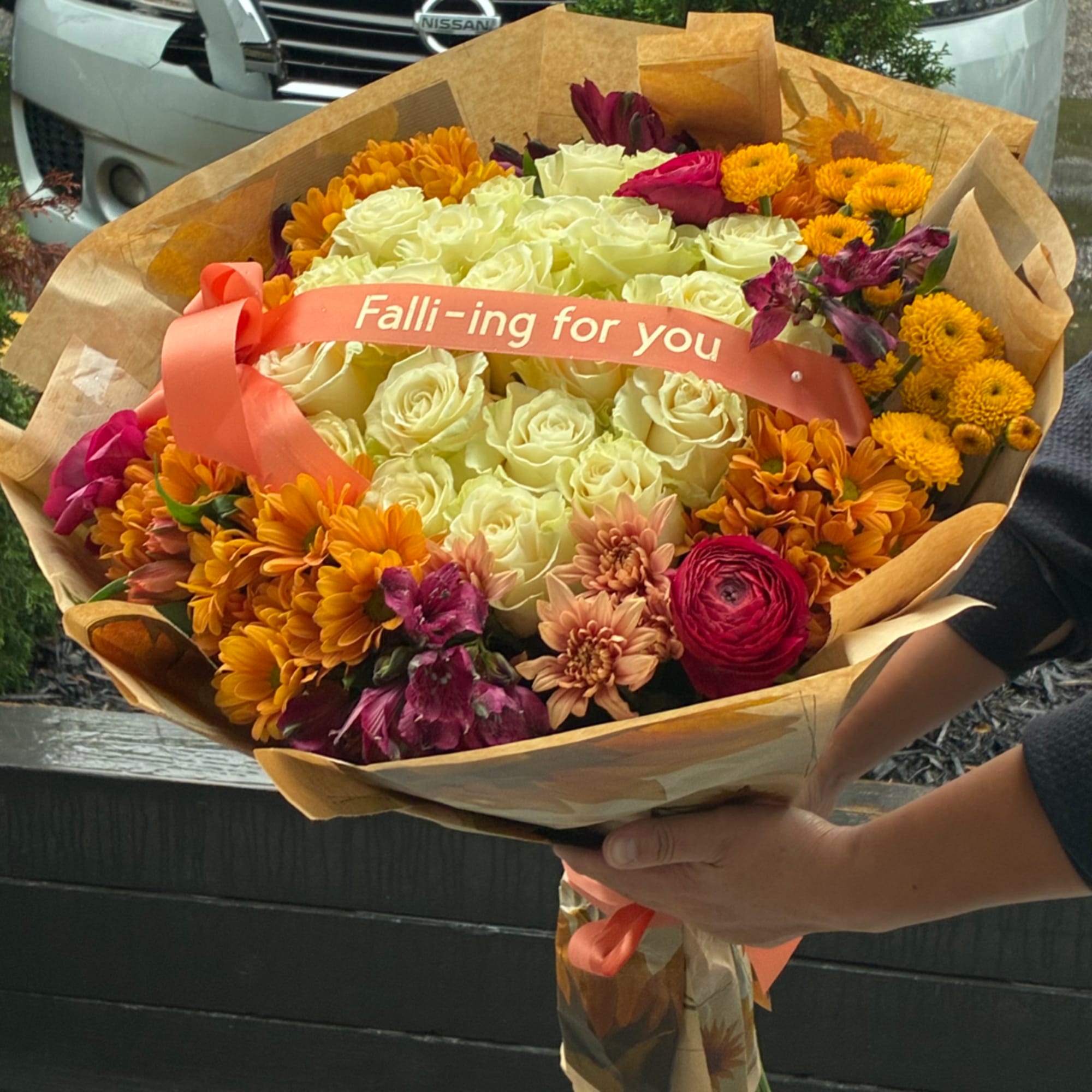 Bouquet of cream roses, orange mums, and pink flowers wrapped in brown paper