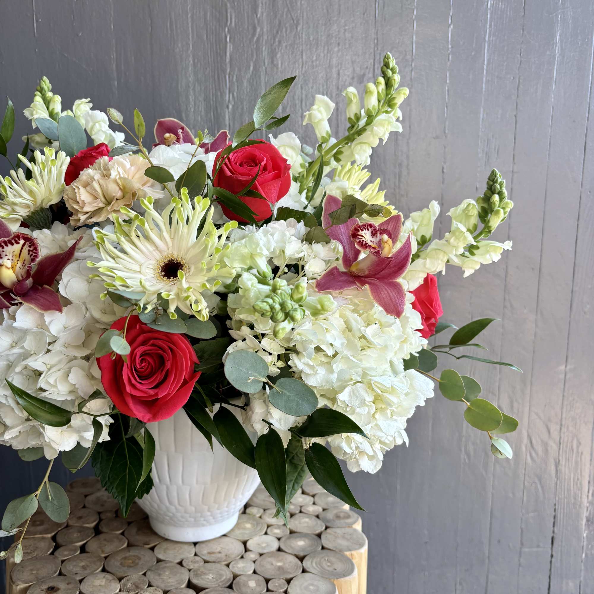 Bouquet of red roses, white hydrangeas, and orchids in a white vase