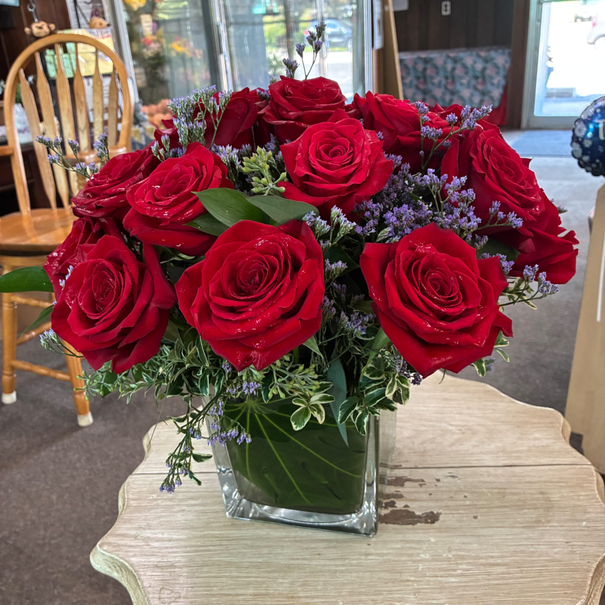 Red roses arranged in a square glass vase with purple filler flowers