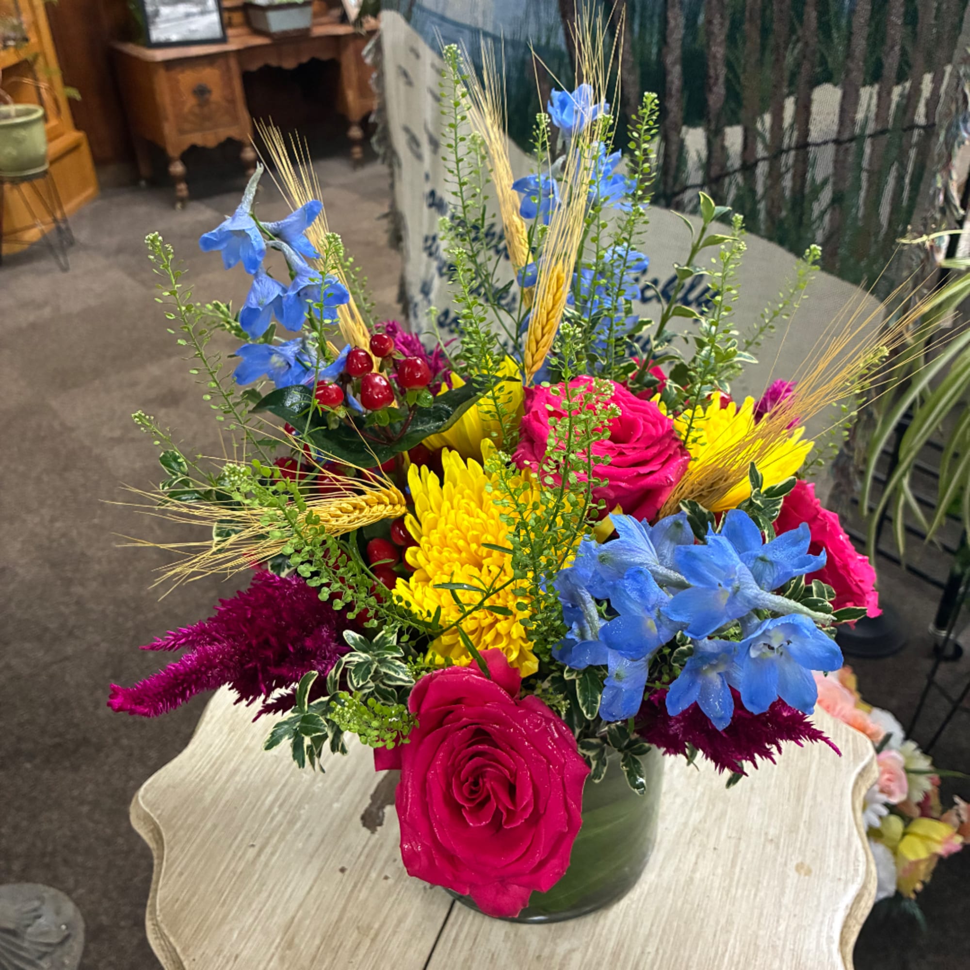Bright mixed bouquet in a green vase with pink roses, yellow mums, and blue flowers