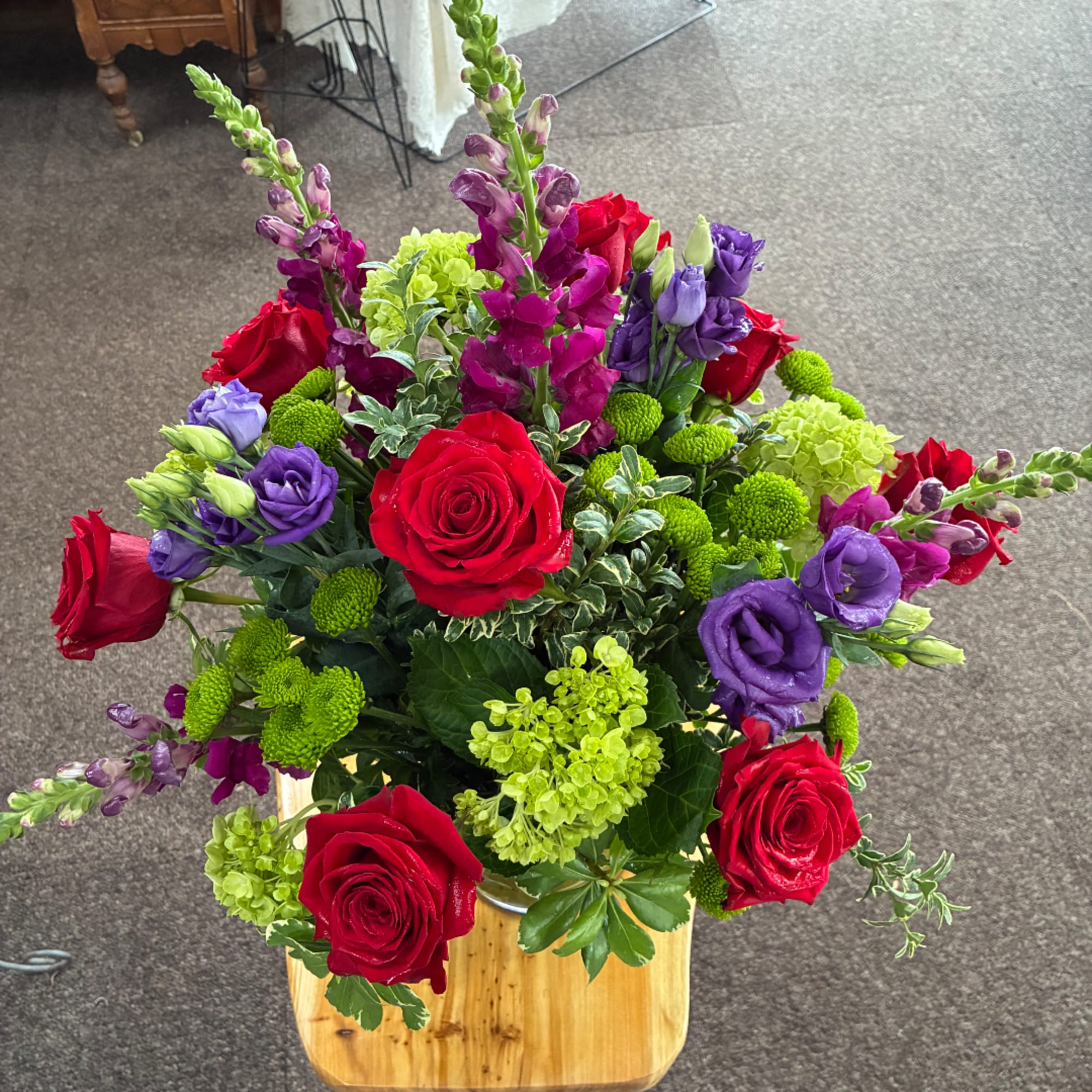 Bouquet of red roses, purple lisianthus, and green hydrangeas in a wooden container