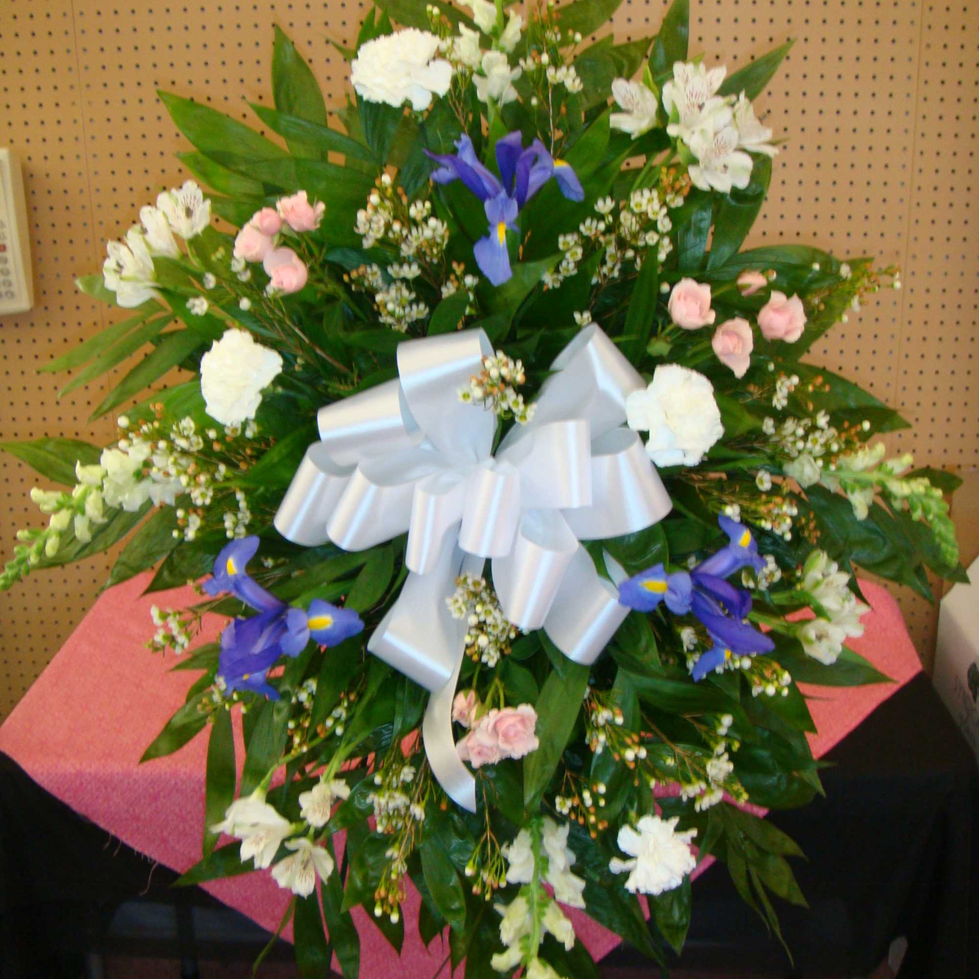 Large standing floral spray with white, pink, and purple flowers and a white bow