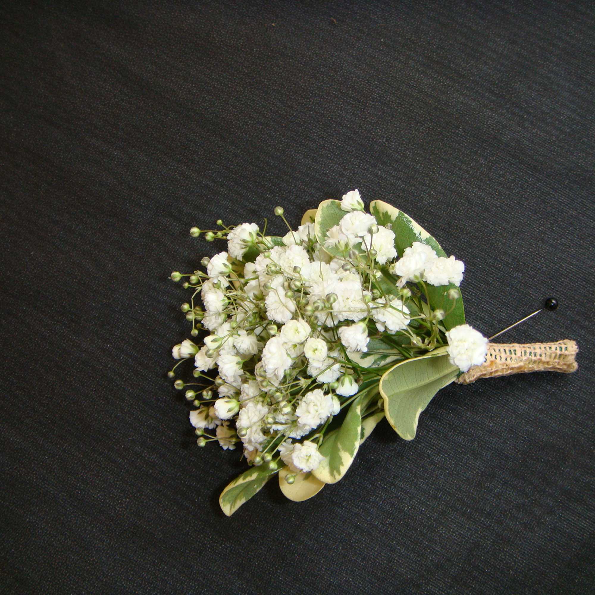 Small white boutonniere with baby's breath and green leaves