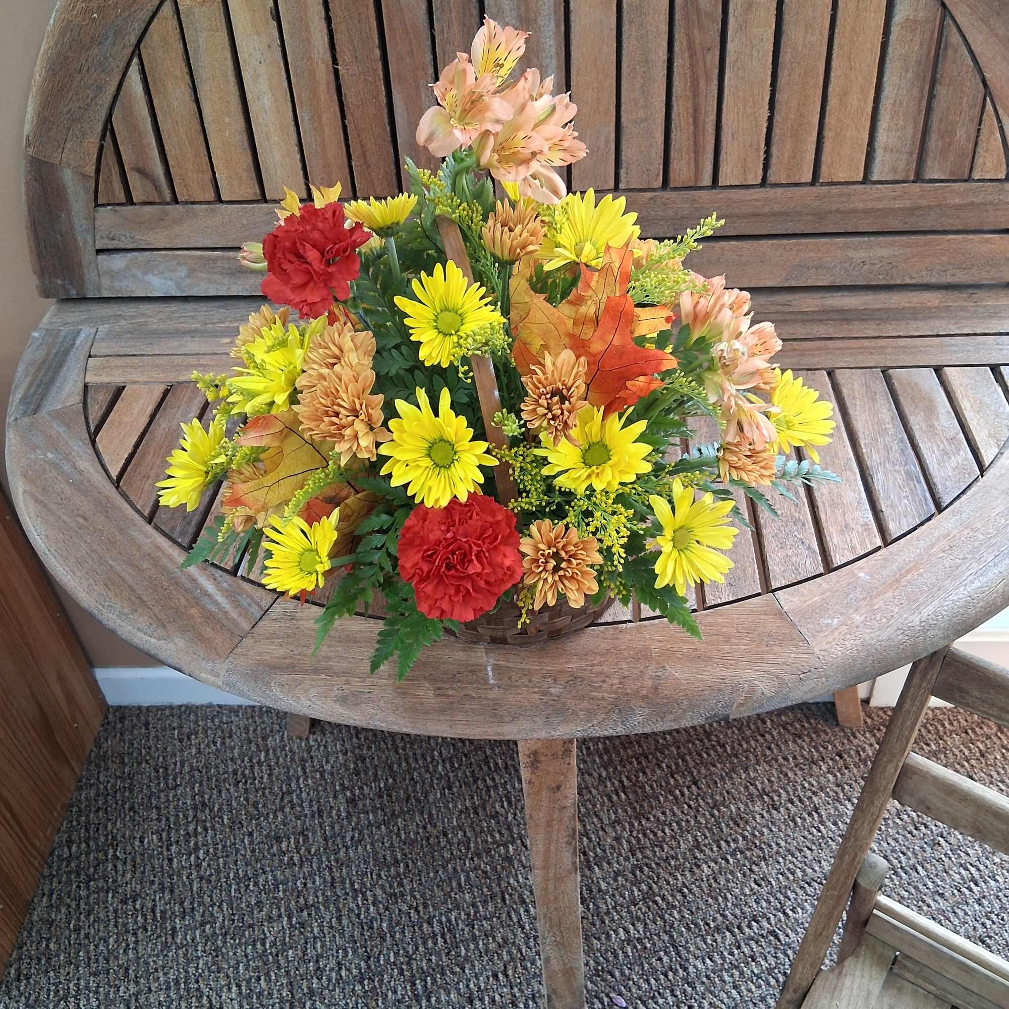Autumn floral arrangement with yellow daisies and red carnations in a basket