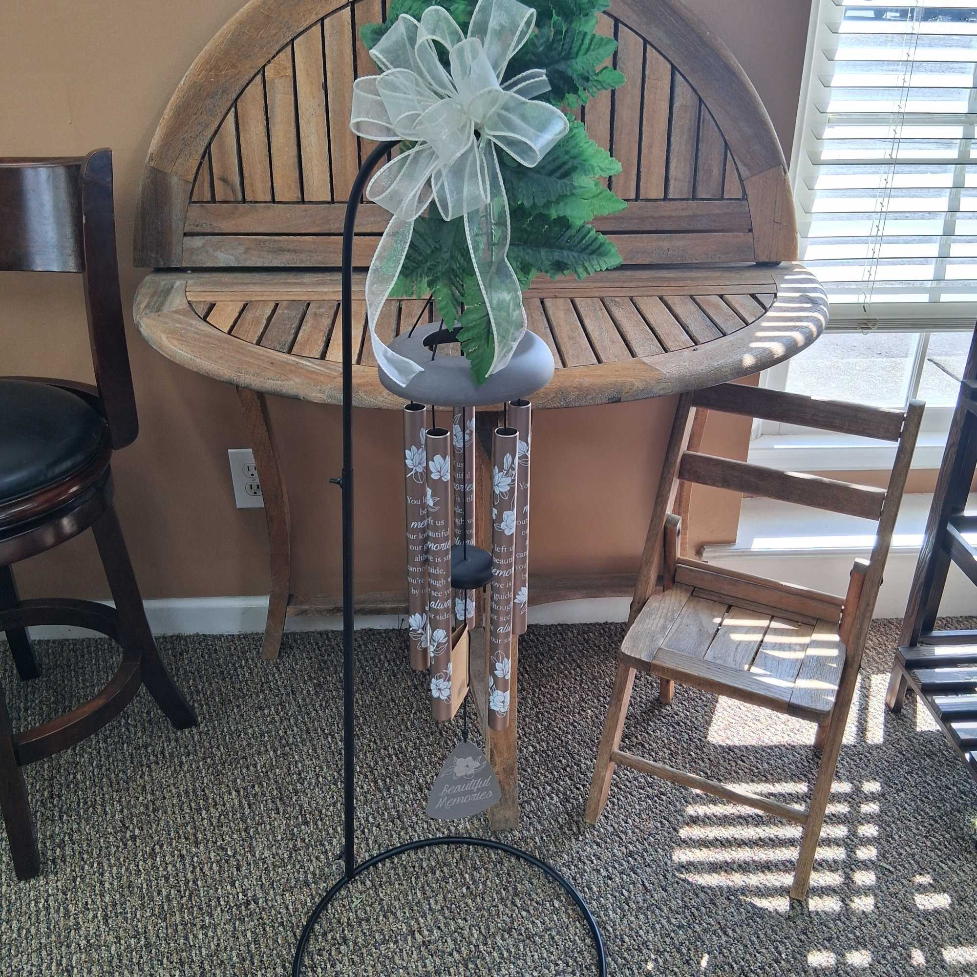Memorial wind chime with faux greenery and a white bow on a metal stand