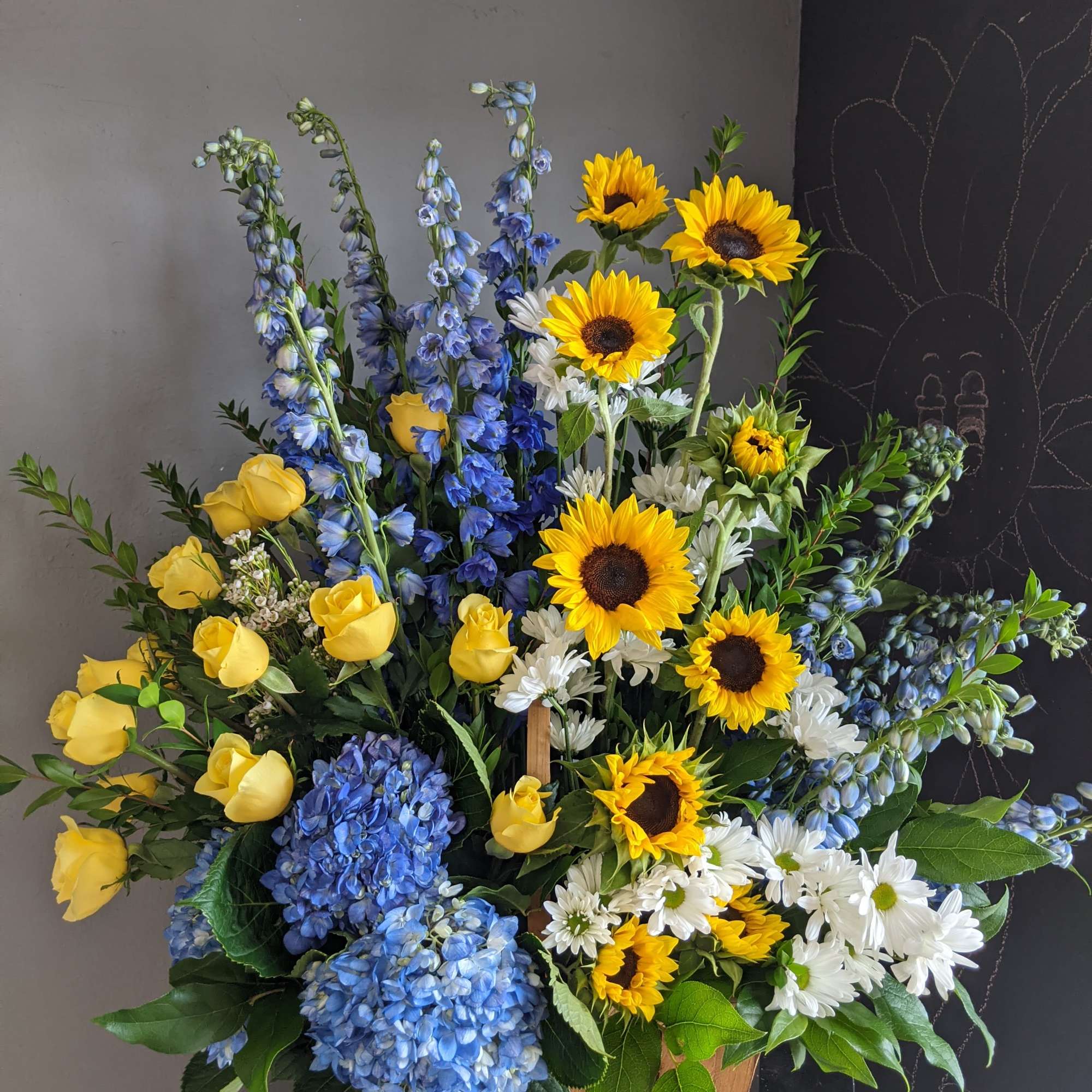 Mixed bouquet with sunflowers, yellow roses, blue hydrangeas, and white daisies