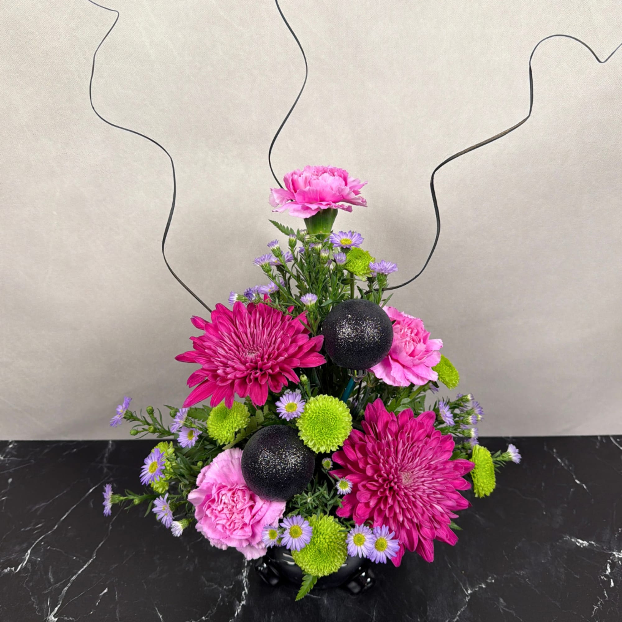 Pink and purple floral arrangement in a black vase with decorative black spheres