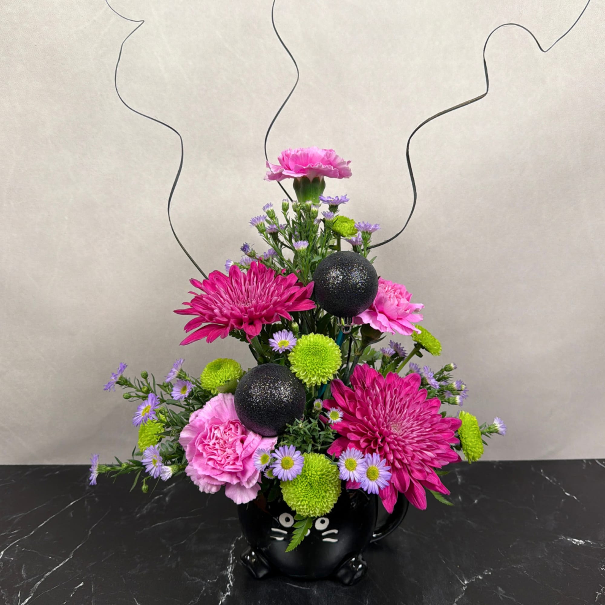 Pink and purple flower arrangement in a black cat mug with glittery black ornaments