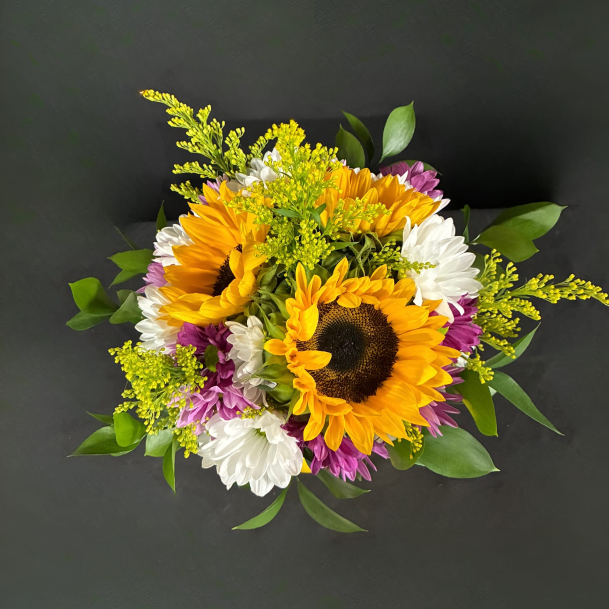Bouquet of sunflowers, white daisies, and purple flowers on a dark background