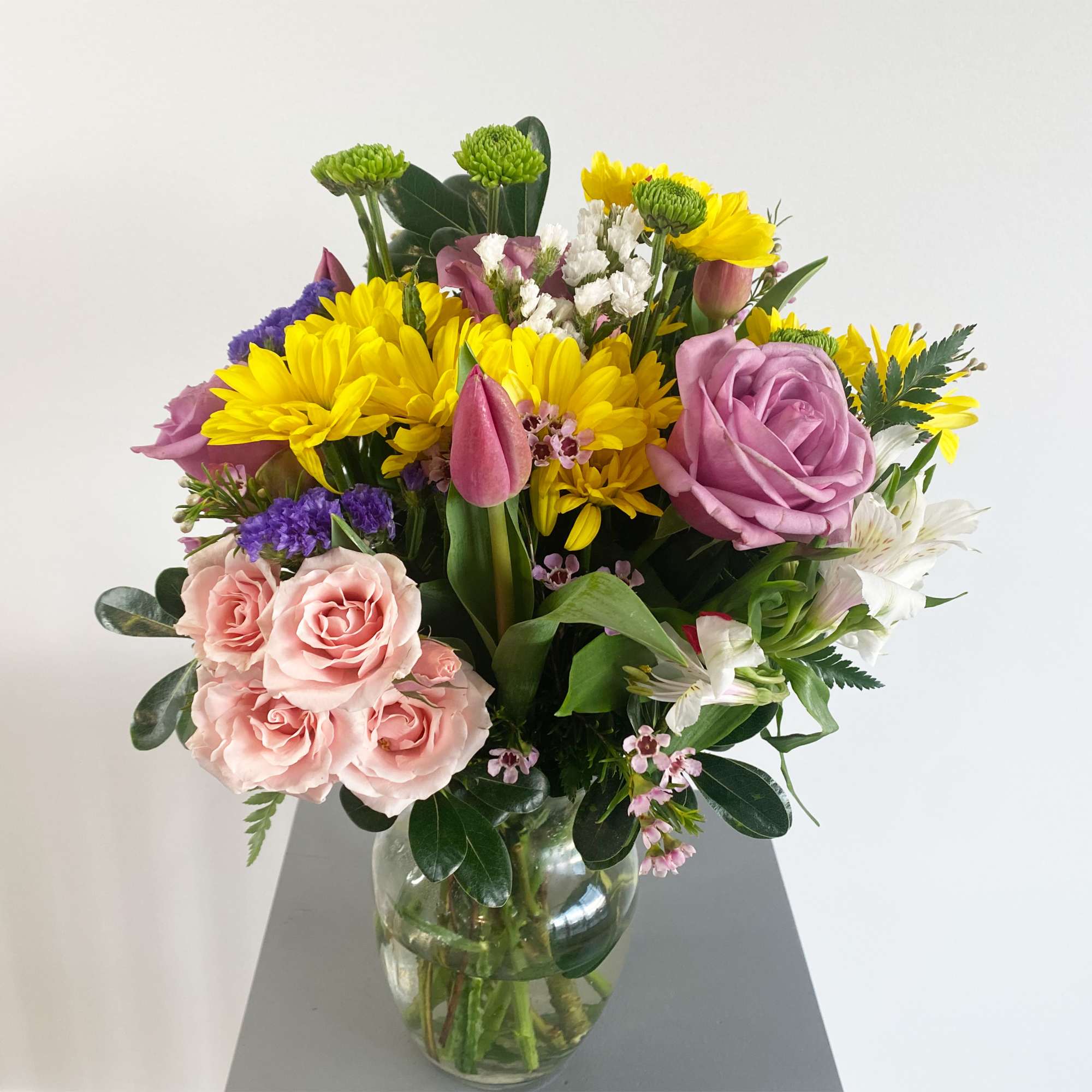 Mixed bouquet of yellow, pink, purple, and white flowers in a glass vase