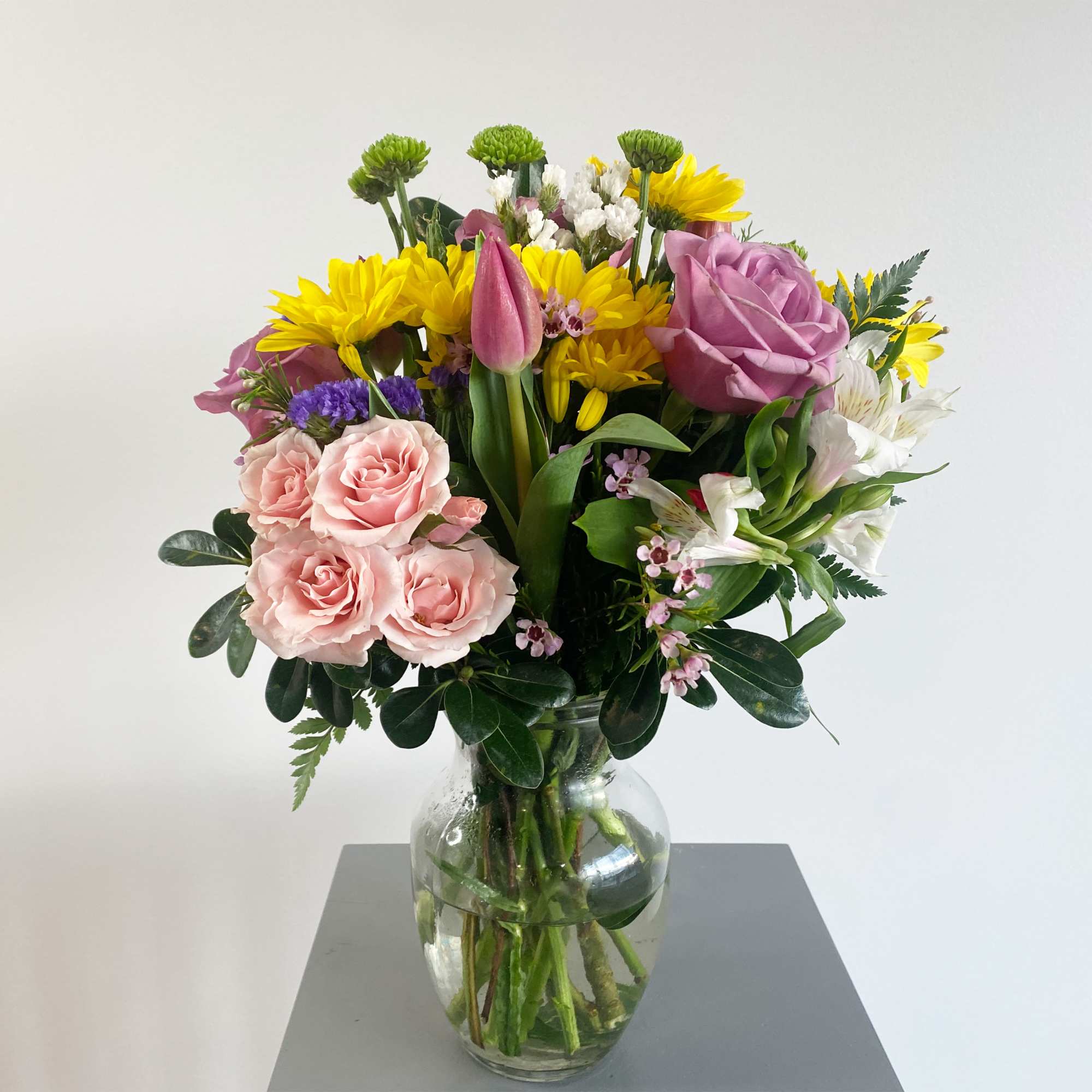 Mixed bouquet of pink, yellow, white, and purple flowers in a glass vase