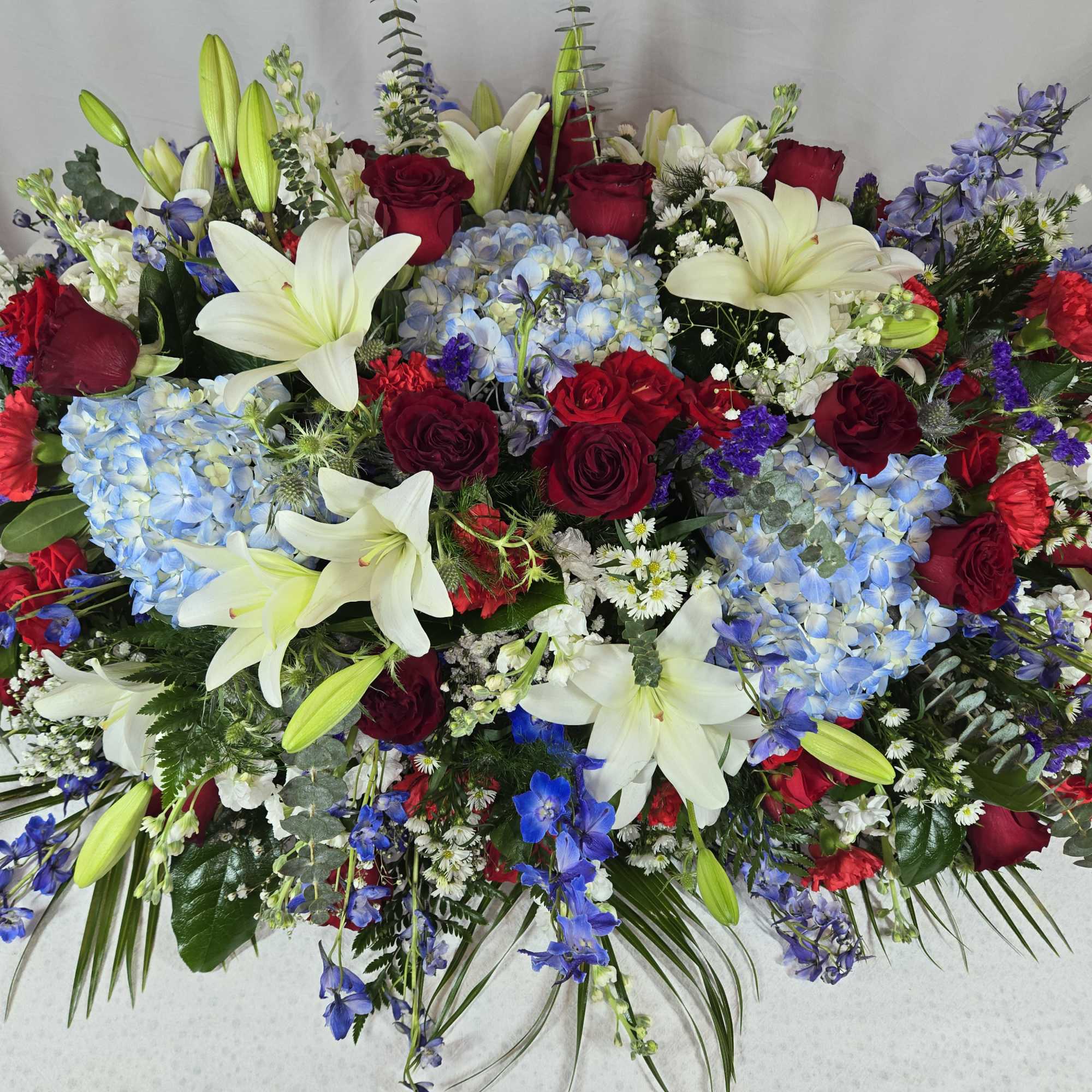 Large casket spray with red roses, white lilies, and blue hydrangeas