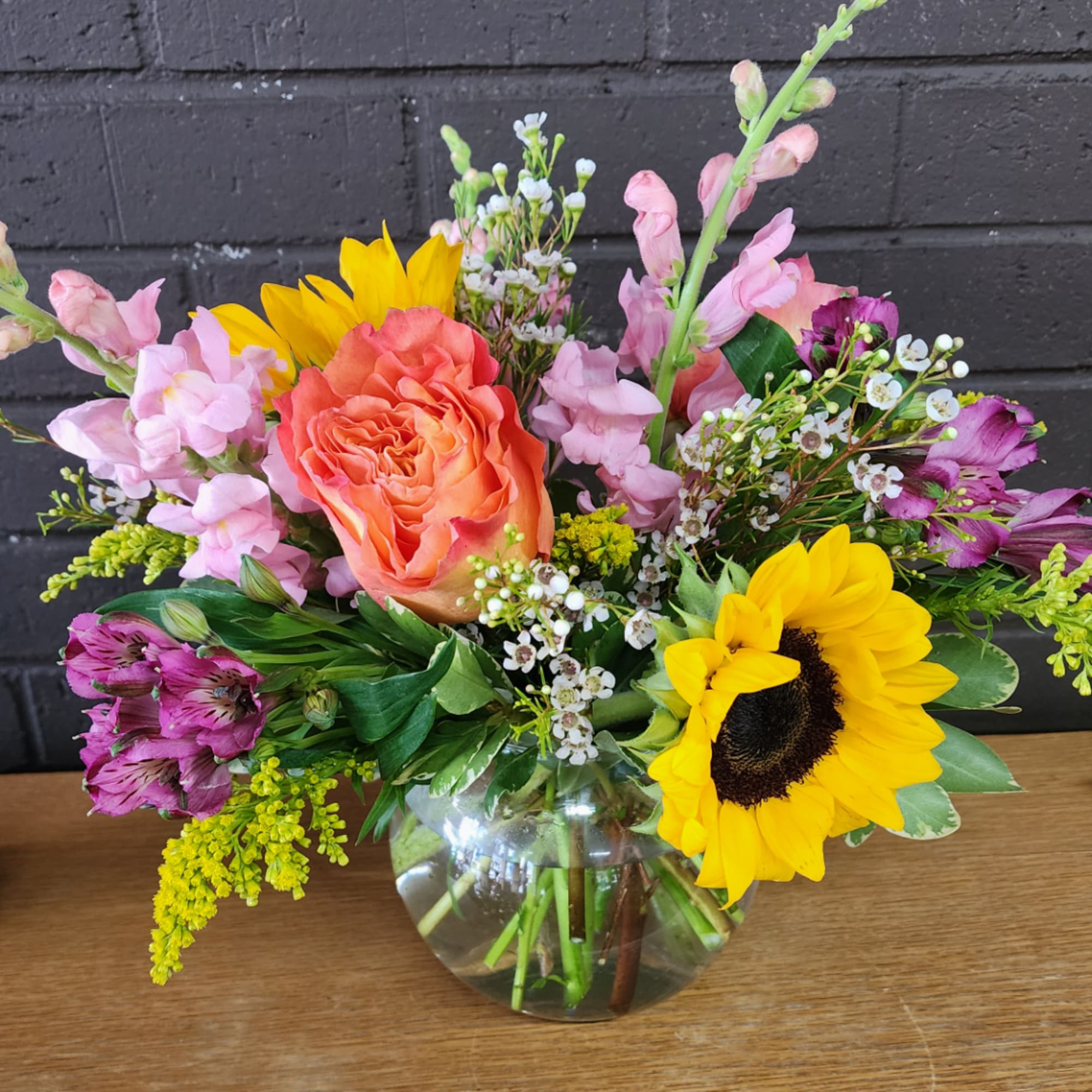 Mixed bouquet in a clear glass vase with sunflowers, a peach rose, and pink blooms