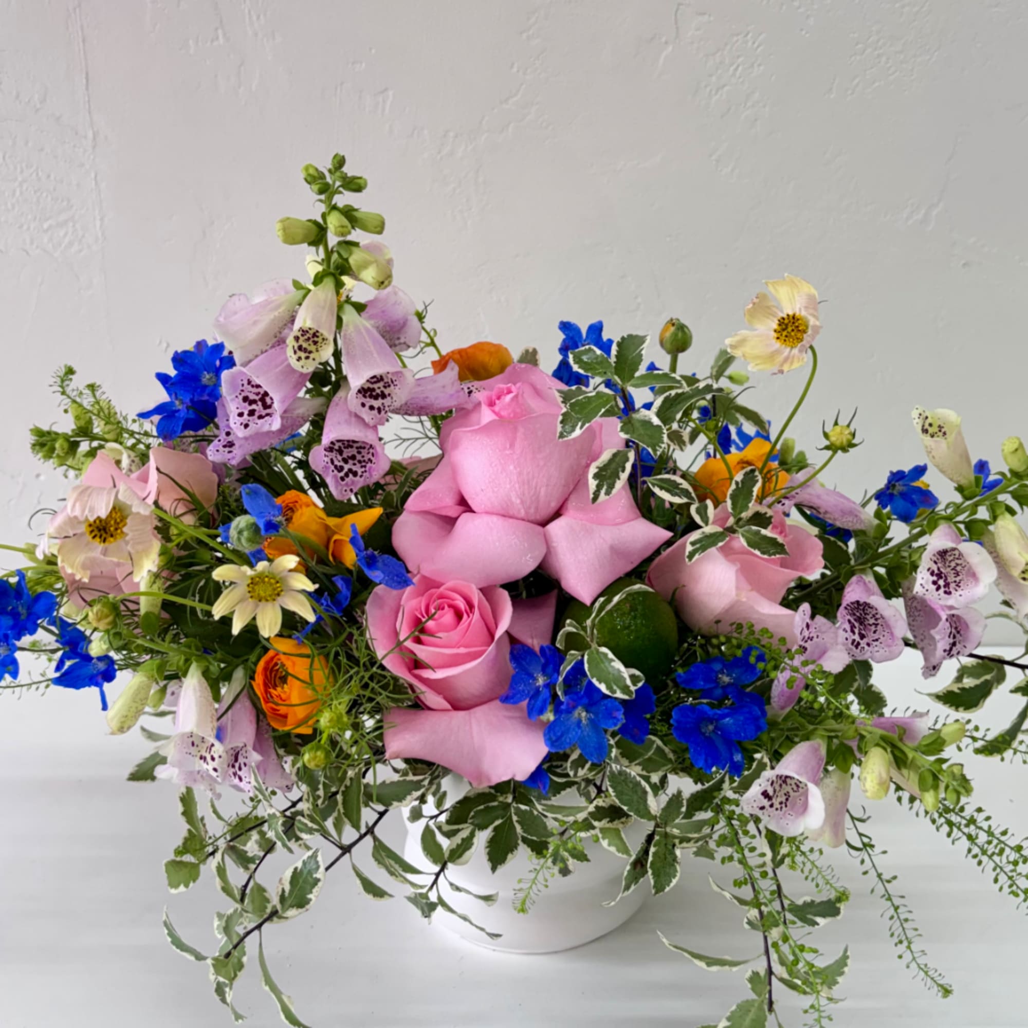Mixed bouquet of pink roses, blue flowers, and pale foxgloves in a white vase