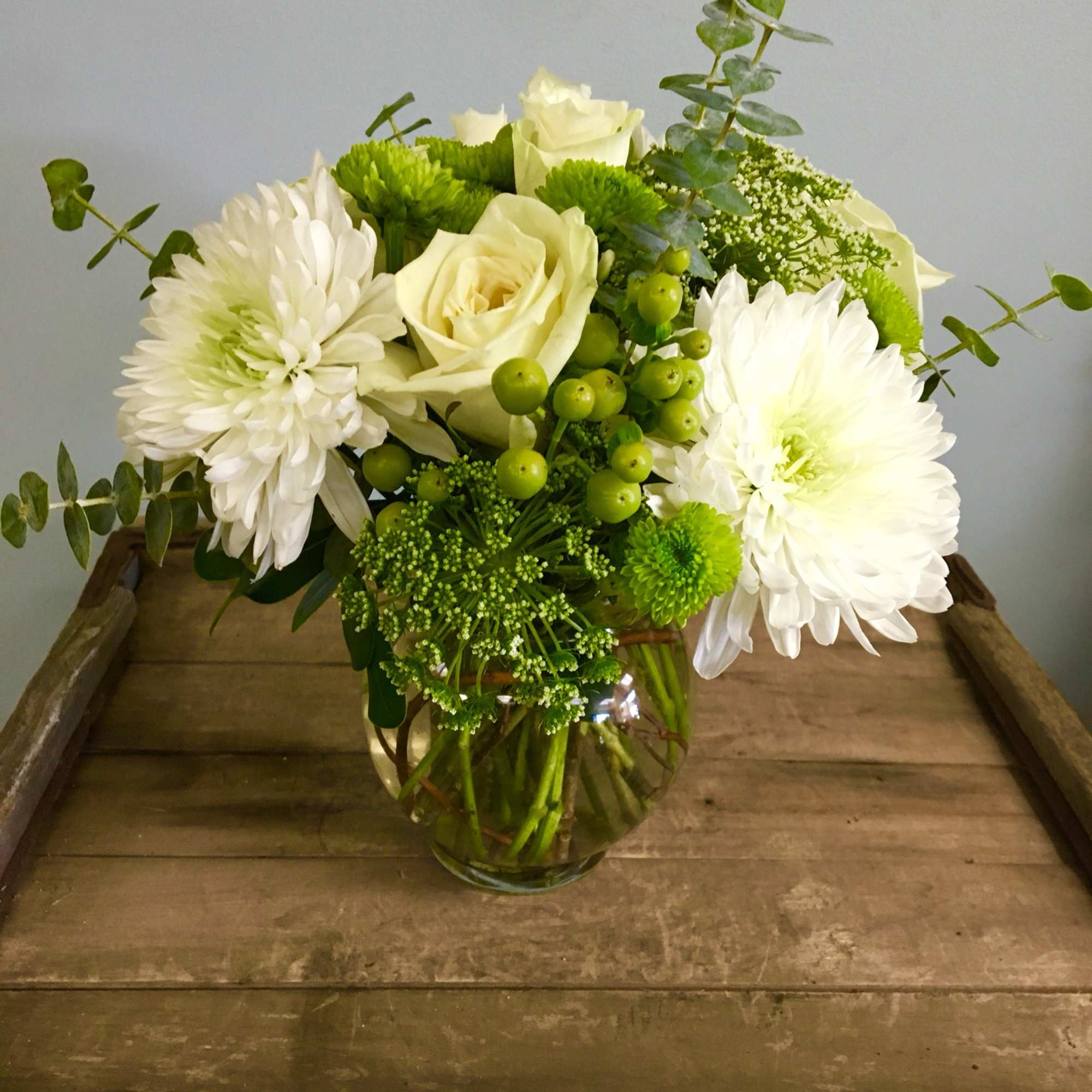 White roses and chrysanthemums in a glass vase with green accents