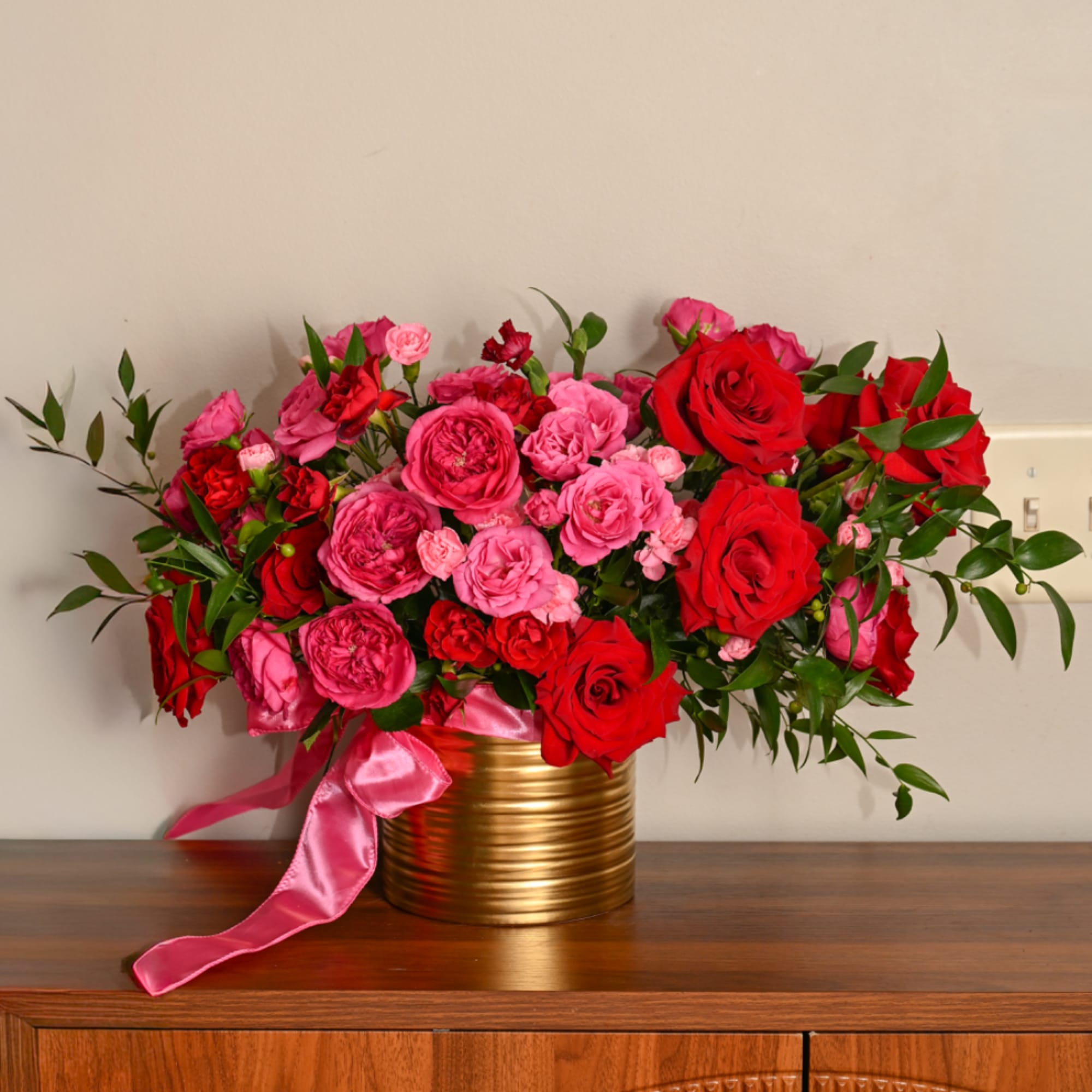 Pink and red roses in a gold vase with a pink ribbon