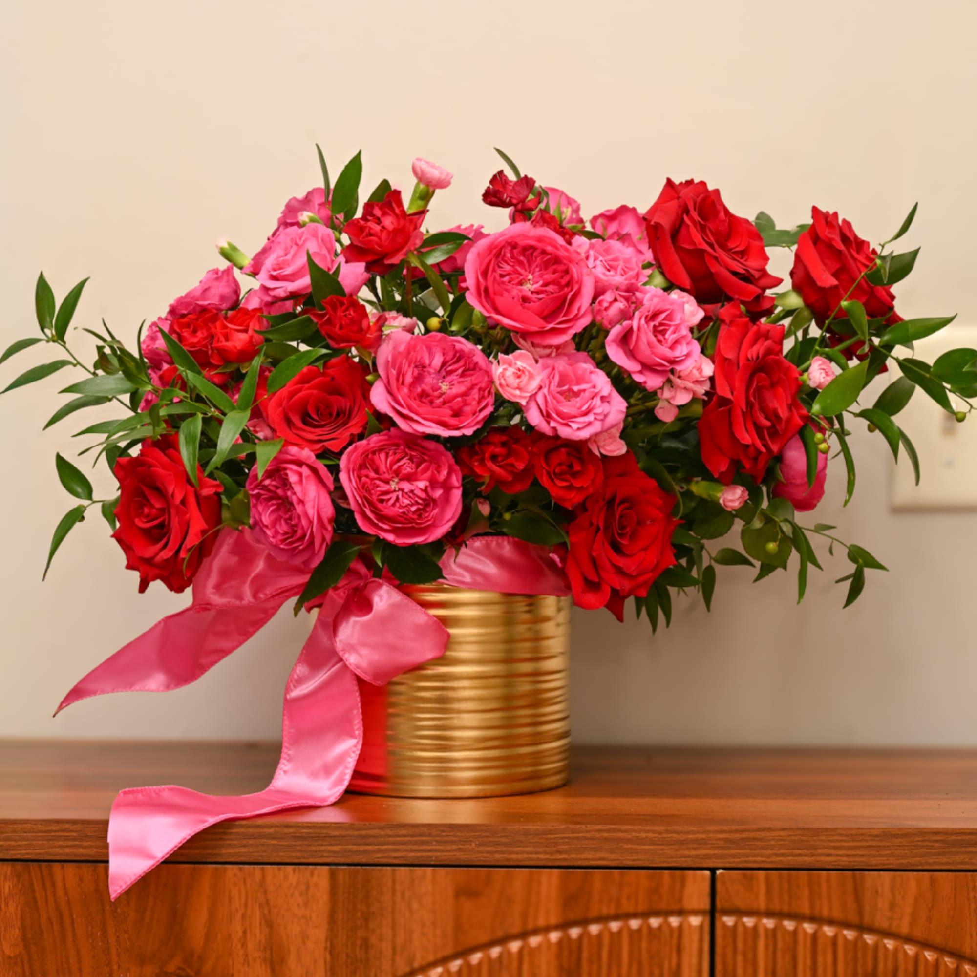 Pink and red roses arranged in a gold tin with a pink ribbon
