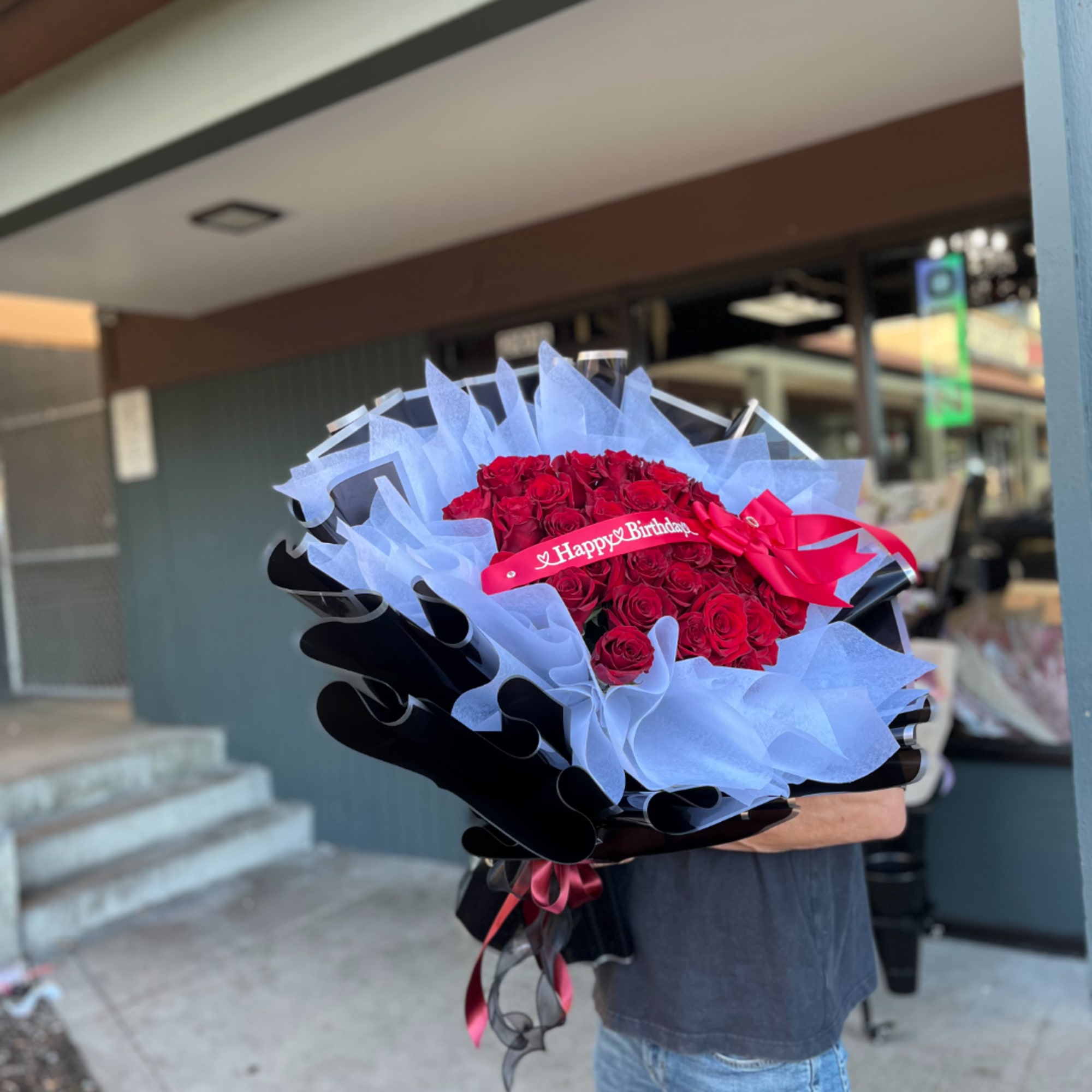 Large bouquet of red roses wrapped in blue and black paper with a birthday ribbon
