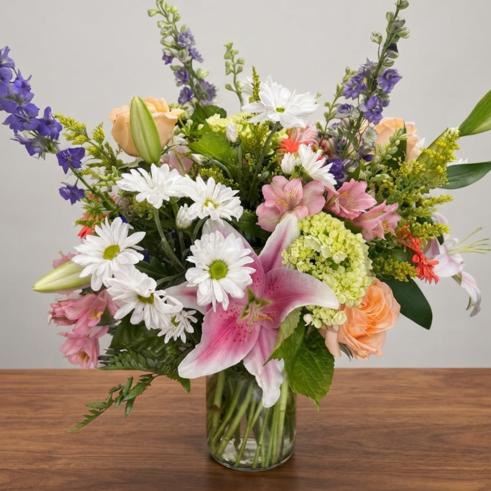 Mixed bouquet in a glass vase with pink lilies, white daisies, and purple flowers