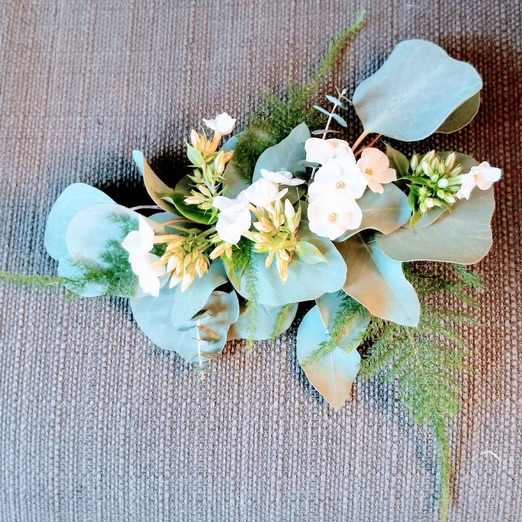 Small floral arrangement with white blossoms and blue-green leaves on a textured surface