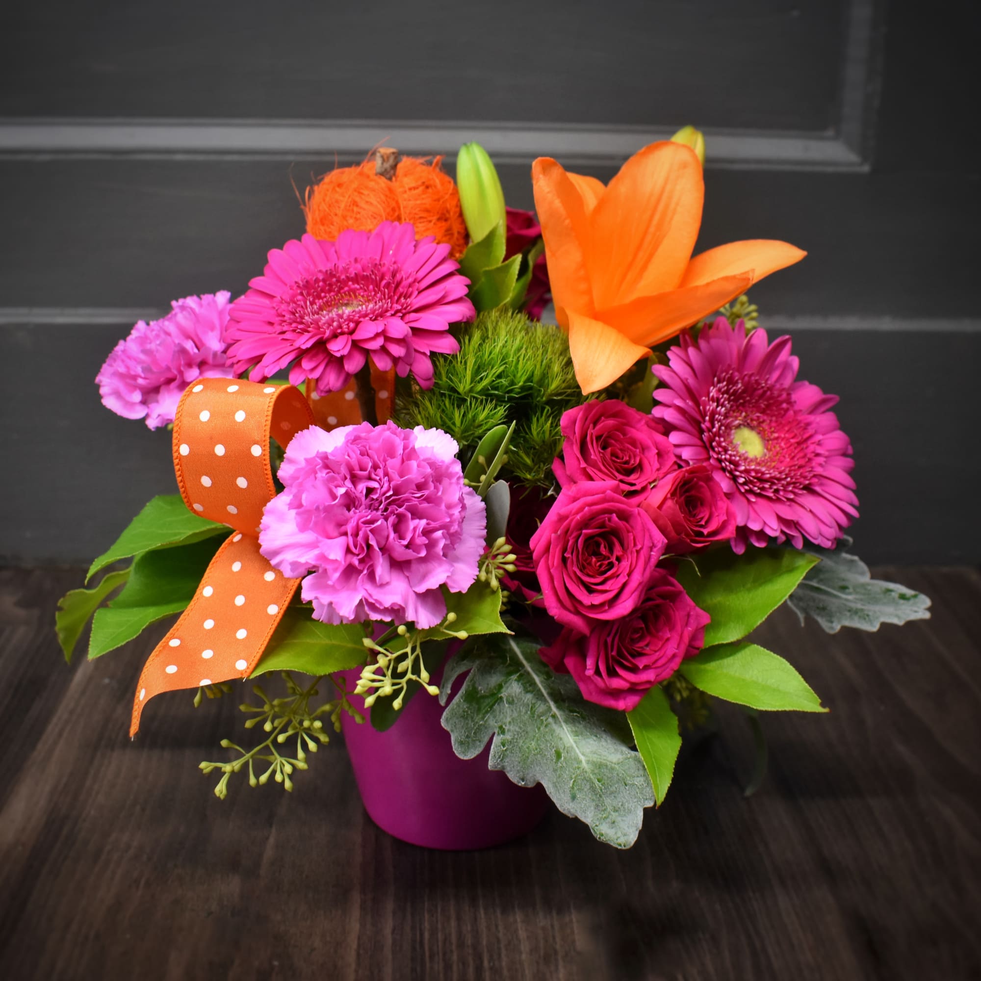 Bright mixed bouquet in a magenta vase with orange ribbon