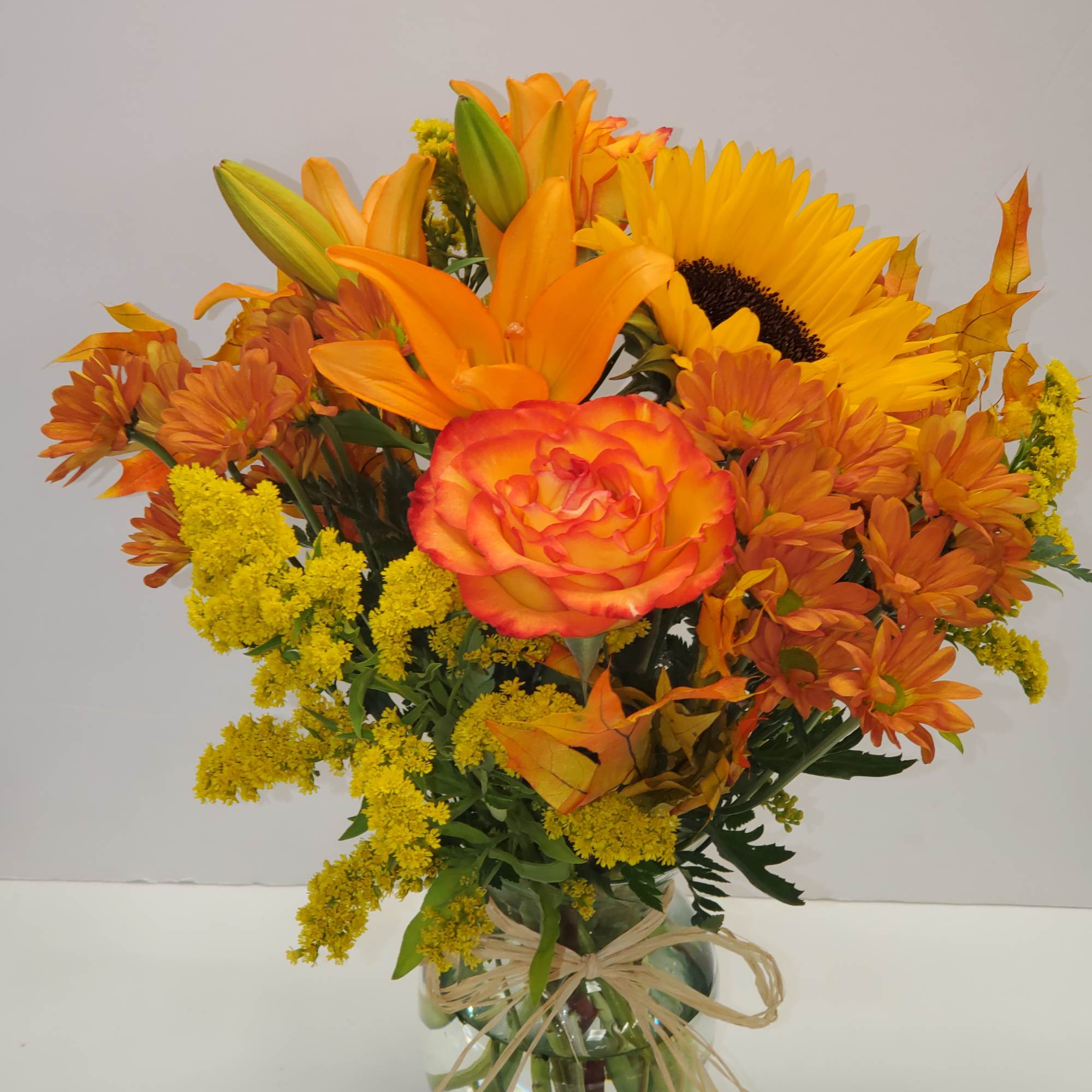 Orange and yellow bouquet in a glass vase with a raffia bow