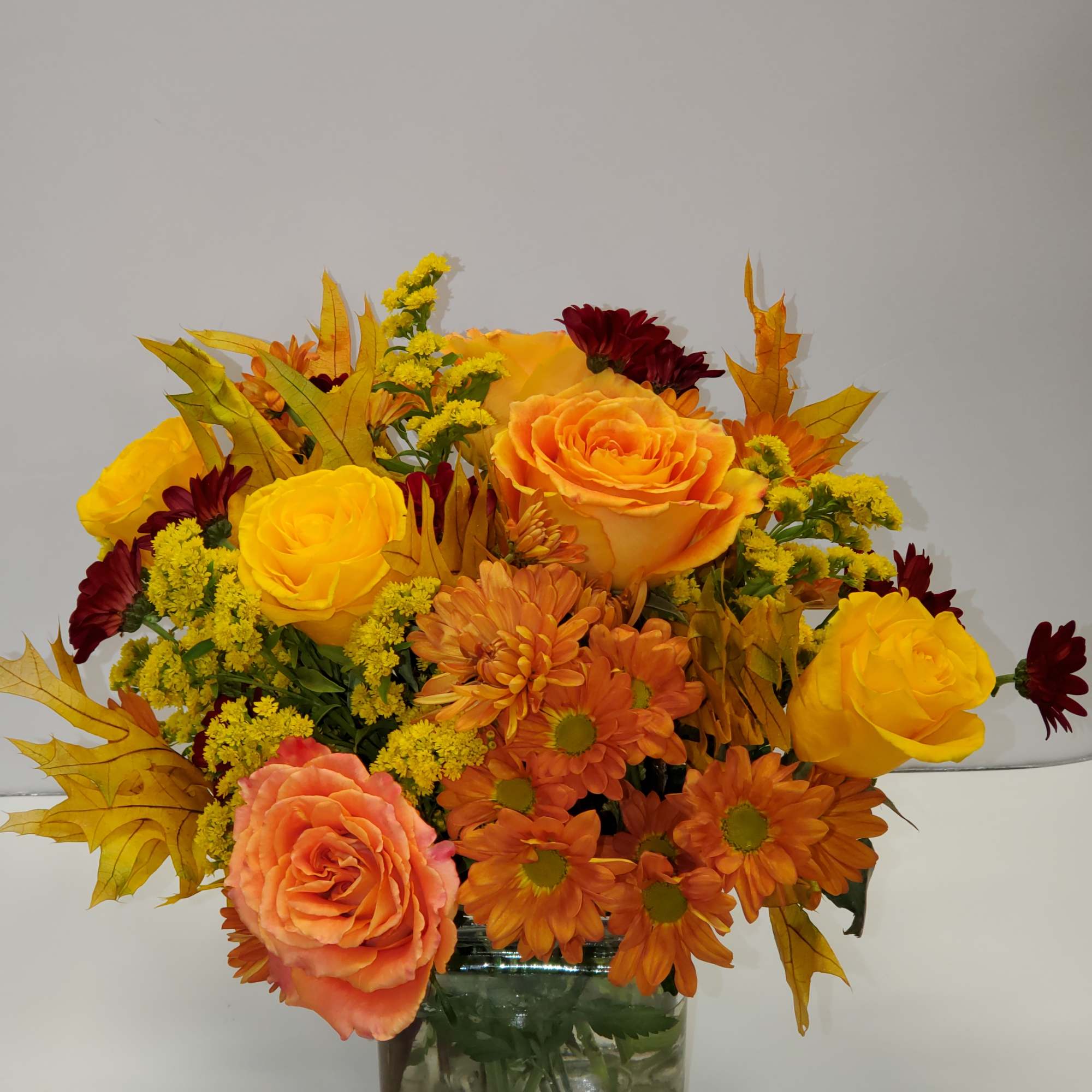 Orange and yellow roses with orange daisies in a glass vase
