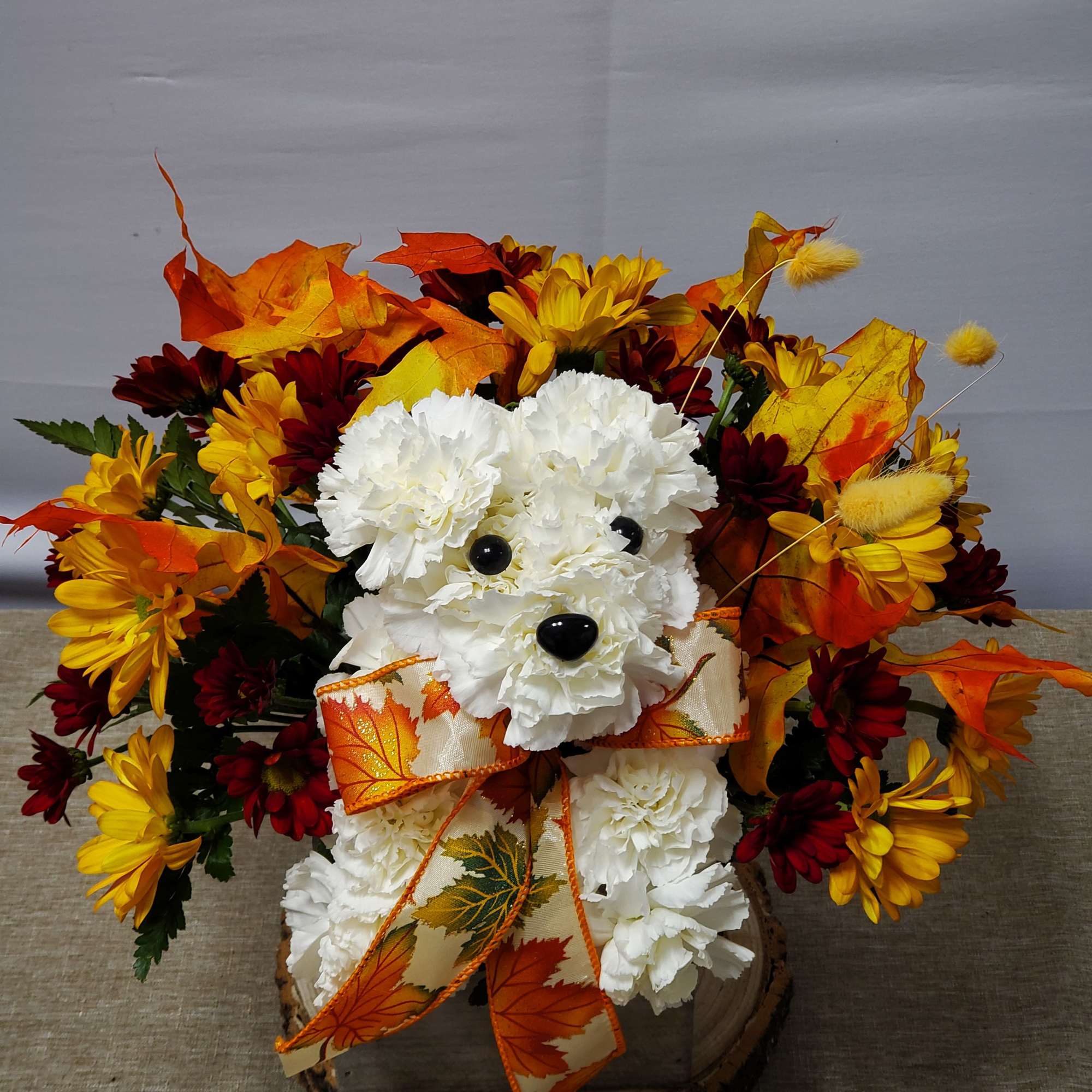 Autumn floral arrangement with a white teddy bear and orange ribbon