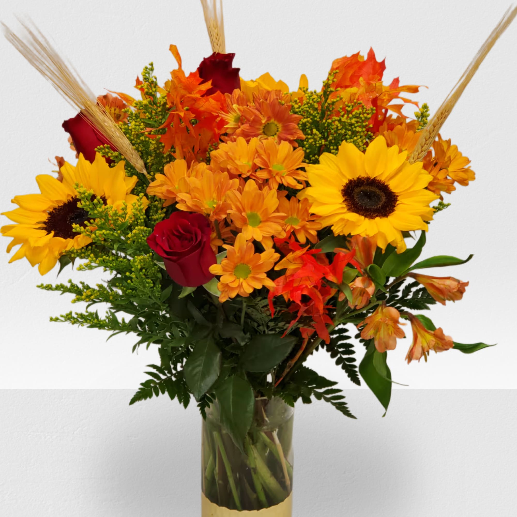 Bouquet of sunflowers, orange daisies, and red roses in a glass vase