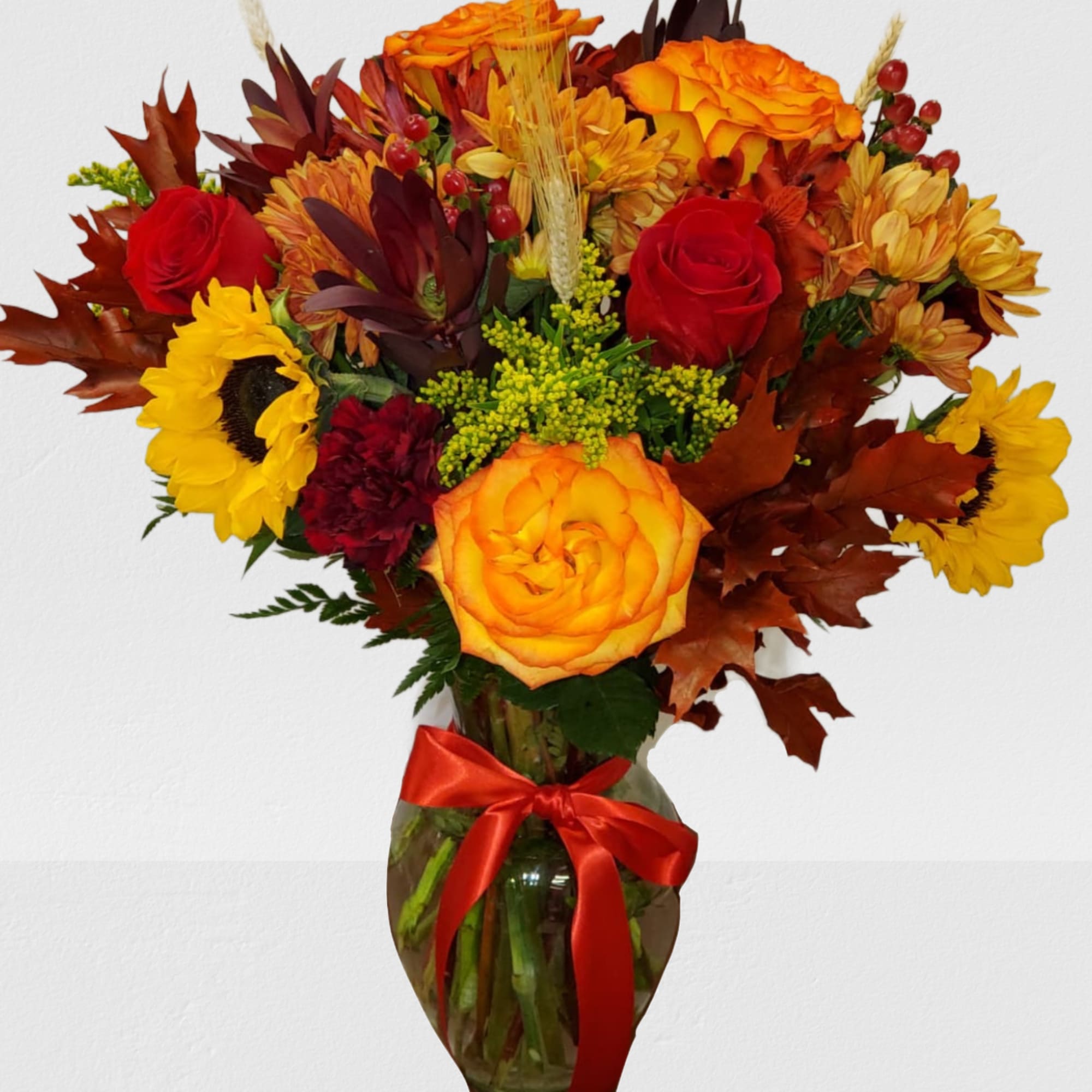 Autumn bouquet of roses, sunflowers, and mums in a glass vase with a red ribbon
