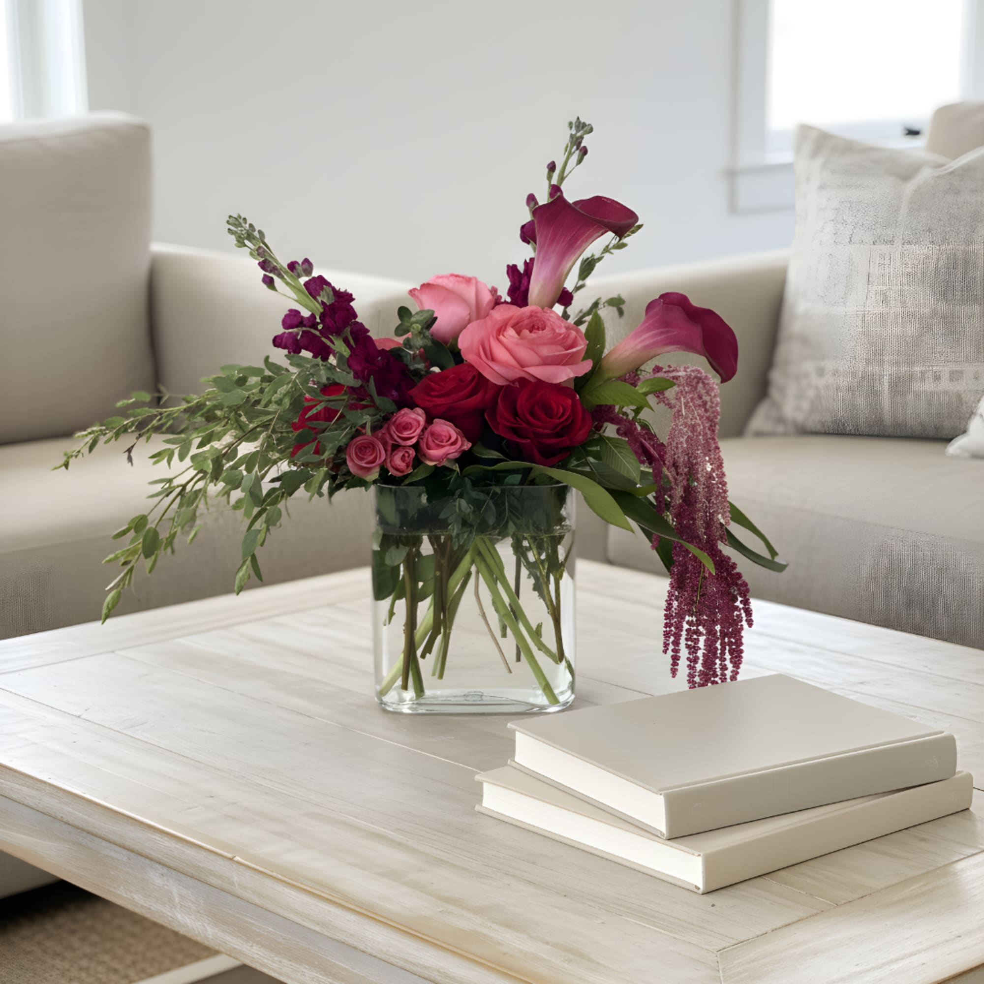 Pink and burgundy floral arrangement in a clear glass vase on a coffee table