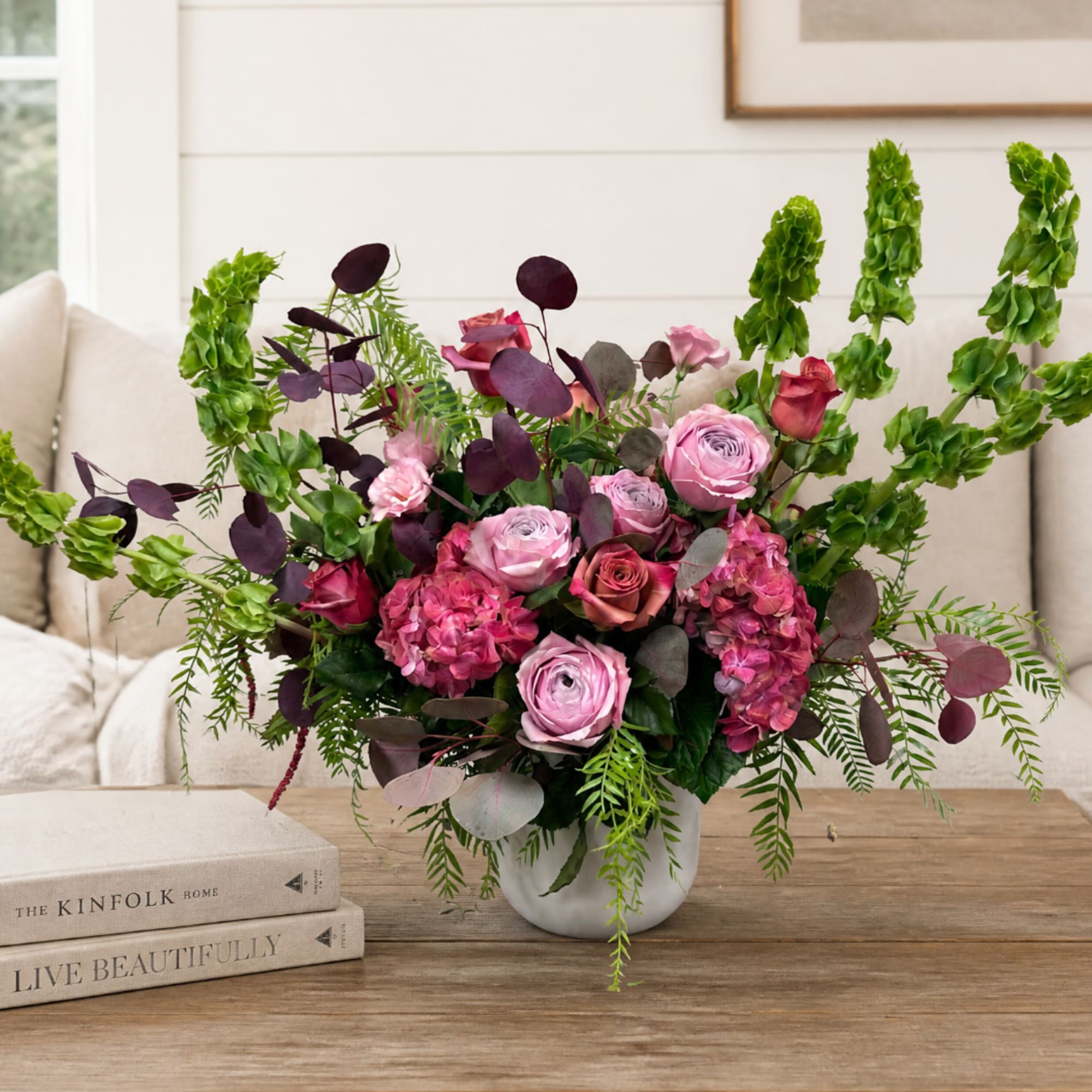 Pink and burgundy floral arrangement in a white vase on a wooden table