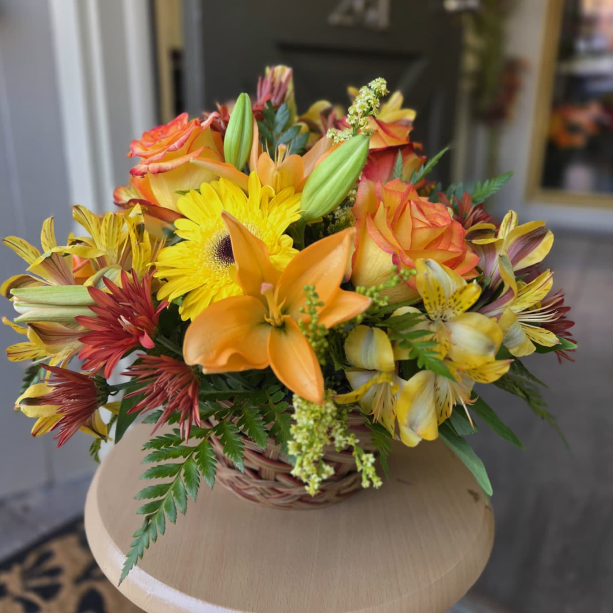 Basket arrangement of orange roses, lilies, and yellow daisies