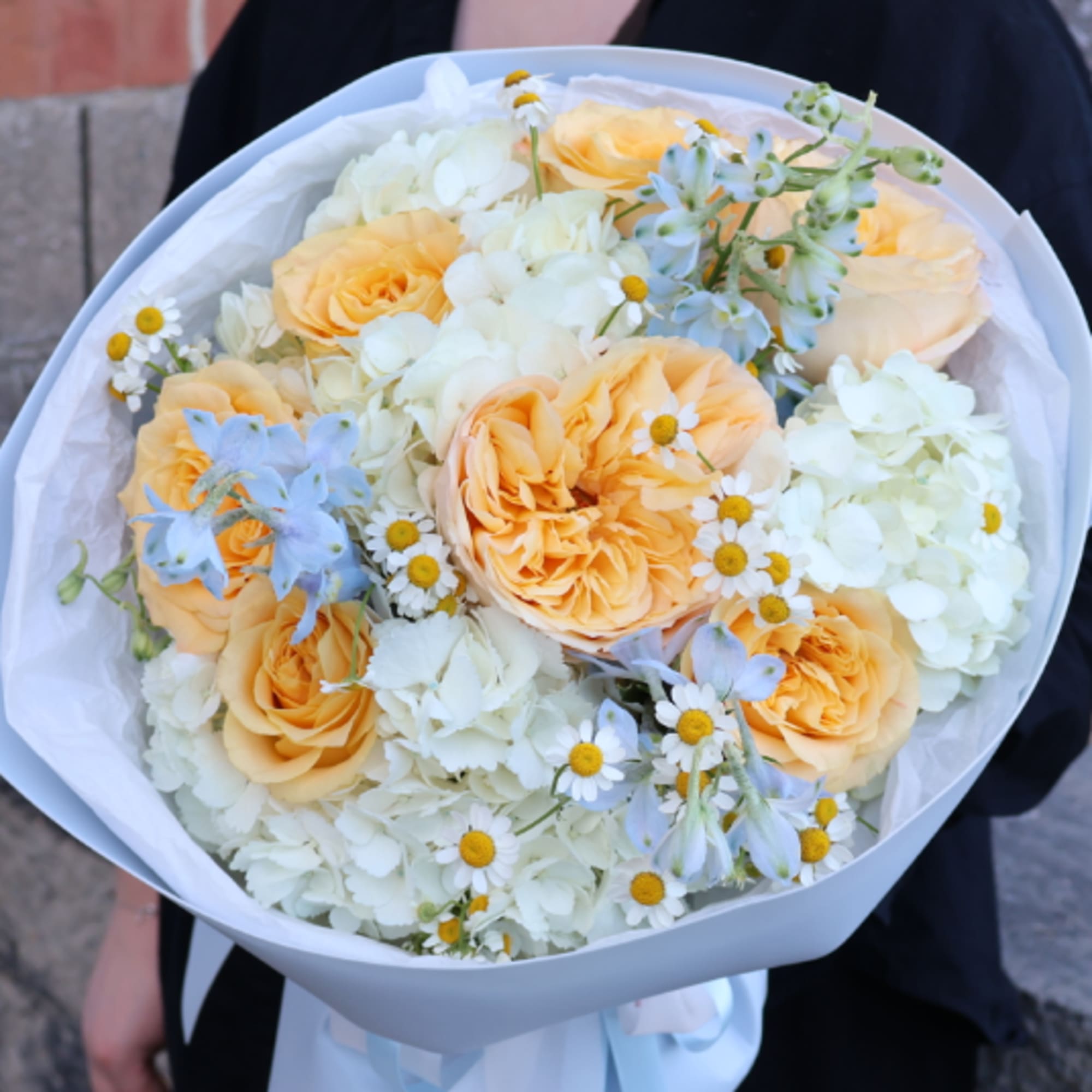 Bouquet of peach roses and white flowers wrapped in pale paper