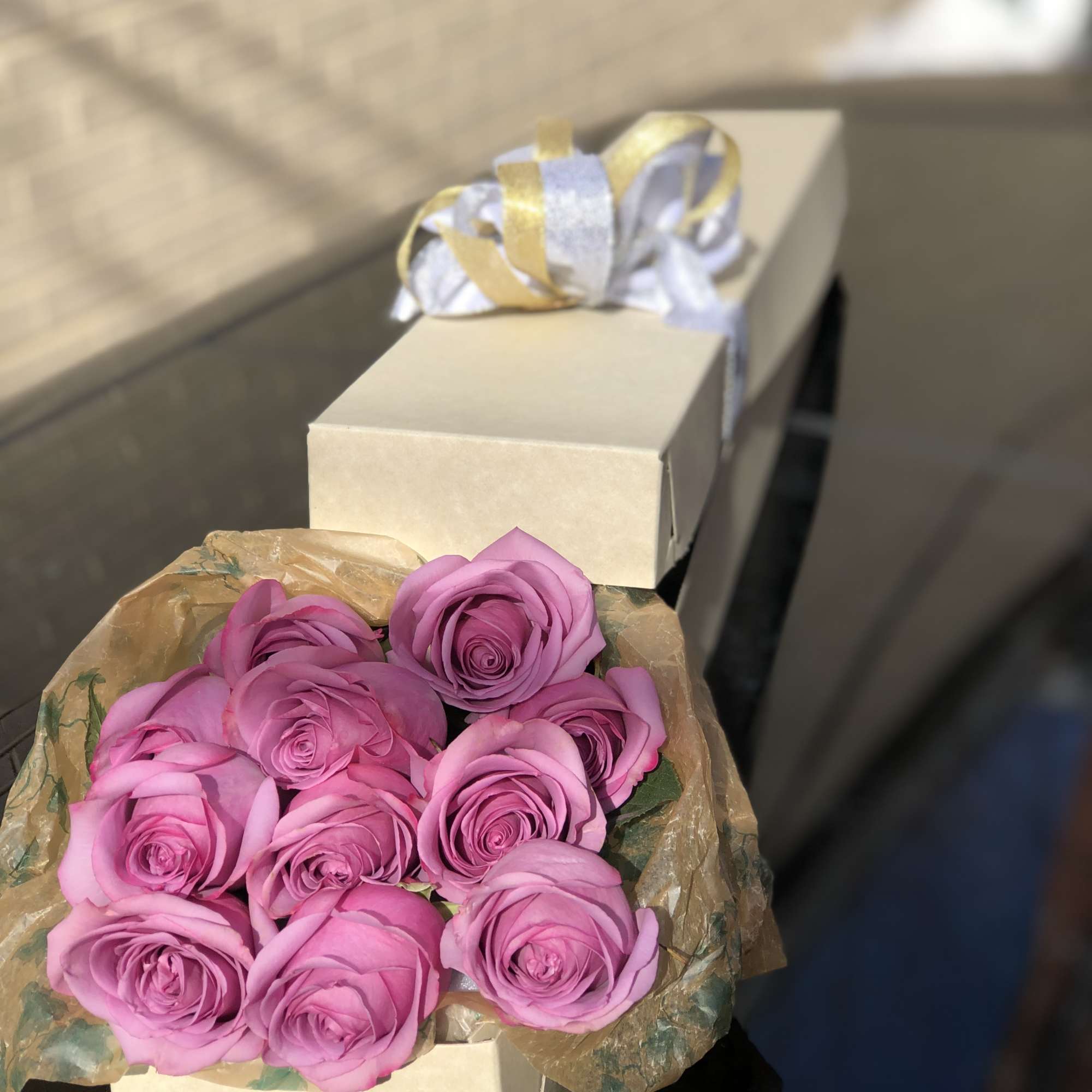 Bouquet of pink roses wrapped in paper beside a cream gift box with ribbon