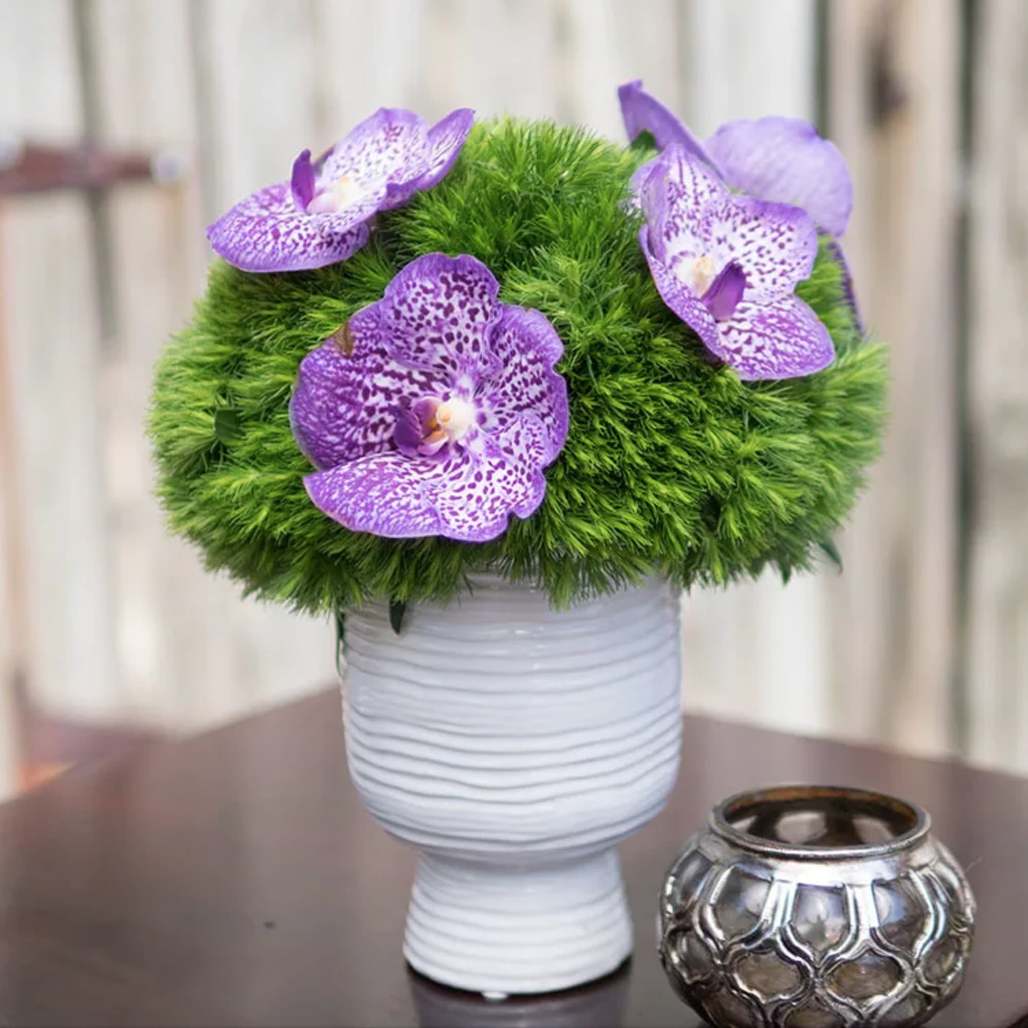 Purple orchids arranged in a white vase with a green moss ball