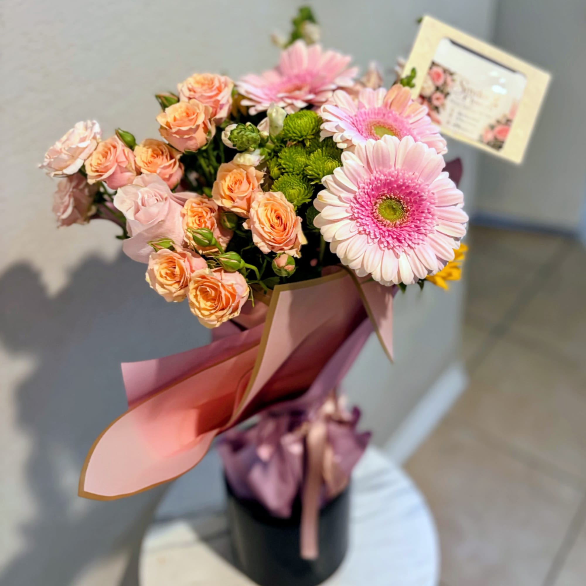 Pink gerbera daisies and peach spray roses in a wrapped bouquet