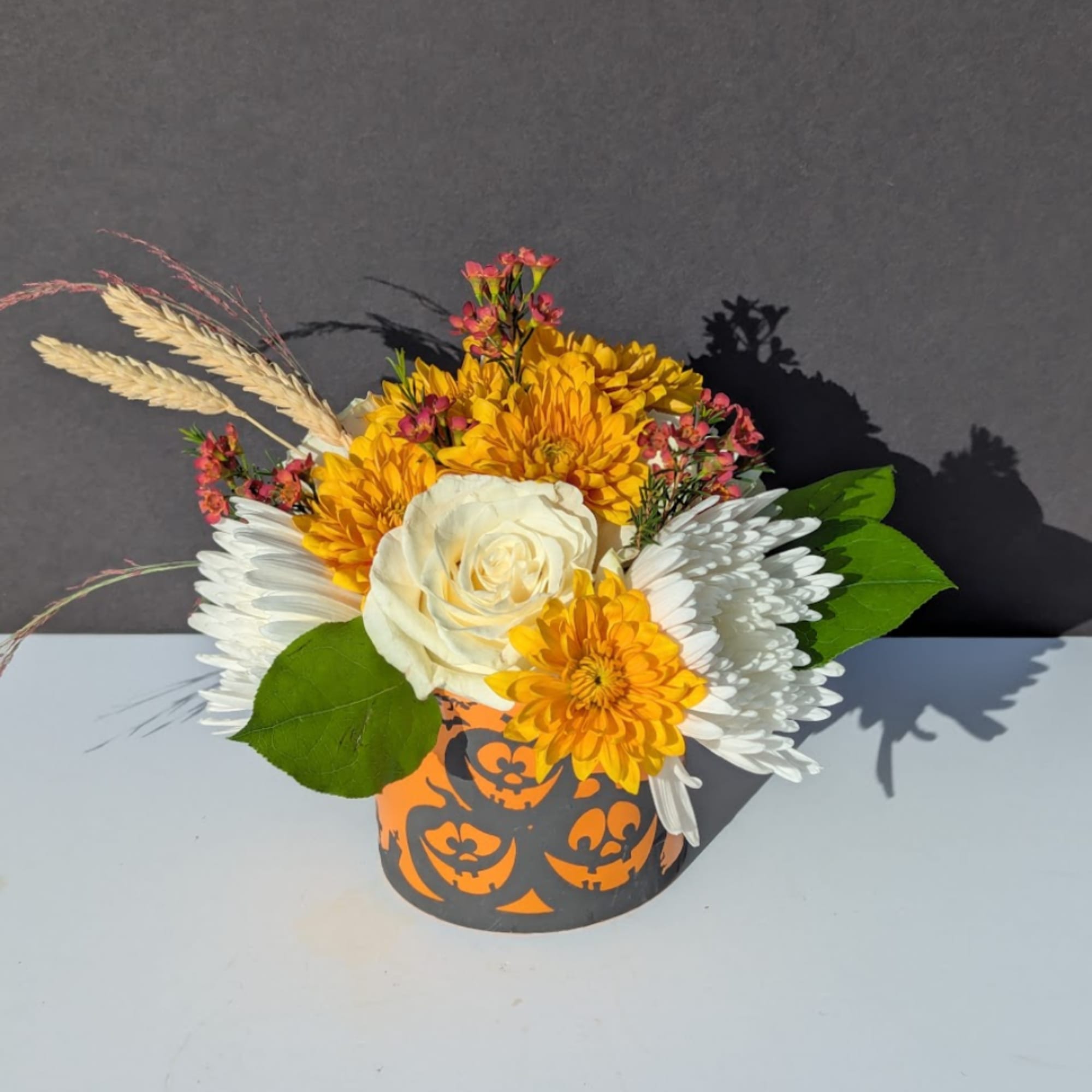 Yellow and white floral arrangement in a Halloween pumpkin container